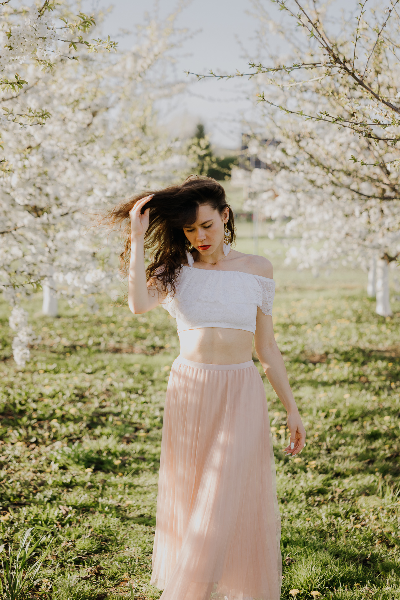 Sesja fotograficzna kobieca w kwitnącym sadzie jabłoniowym pod Krakowem, modelka pośród białych kwiatów wiosną, profesjonalna fotografia plenerowa, Małopolska