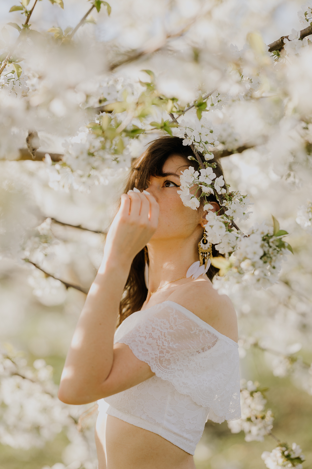 Sesja fotograficzna kobieca w kwitnącym sadzie jabłoniowym pod Krakowem, modelka w białej bluzce pośród białych kwiatów wiosną, profesjonalna fotografia plenerowa, Małopolska