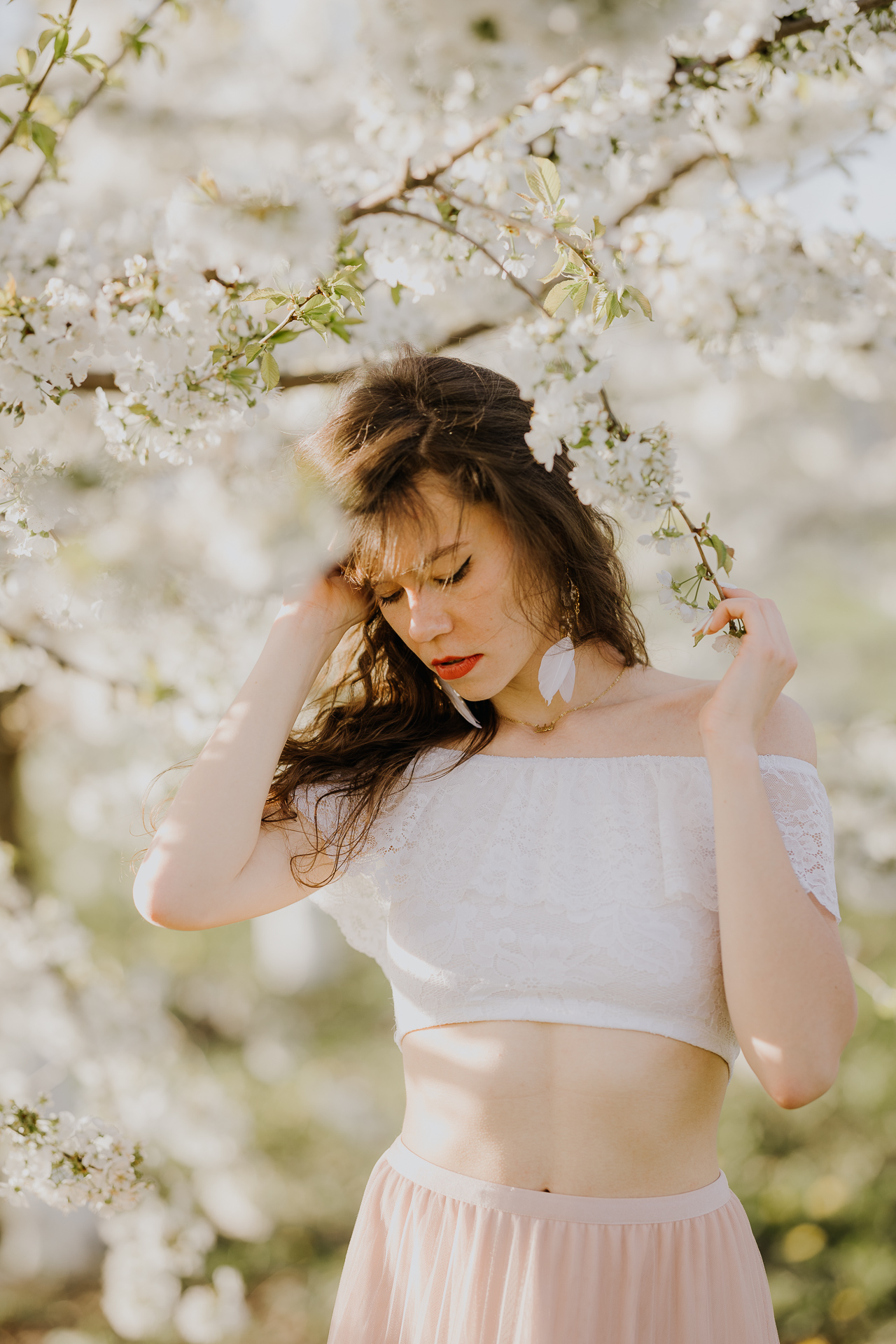 Zbliżenie twarzy modelki podczas sesji w kwitnącym sadzie jabłoniowym, profesjonalna fotografia kobieca, okolice Krakowa