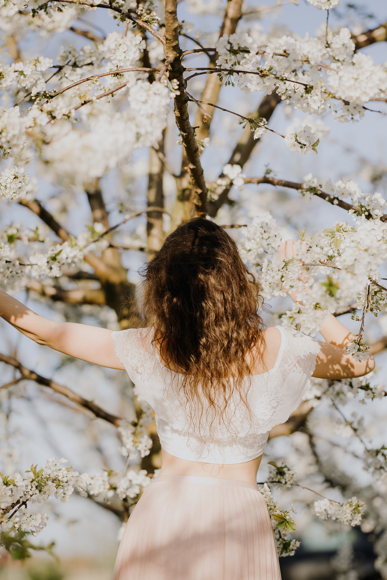 Kobieta obrócona plecami na tle kwitnących drzew owocowych, sesja fotograficzna wiosenna w sadzie pod Krakowem