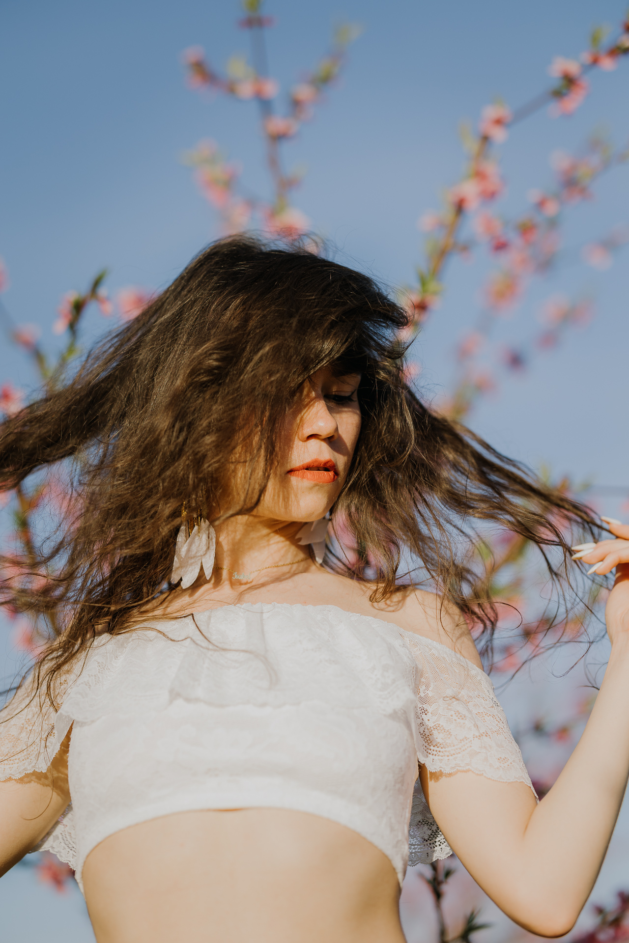 Portret kobiety w kwitnącym sadzie pod Krakowem, modelka na tle brzoskwini w pełnym rozkwicie, wiosenna sesja fotograficzna