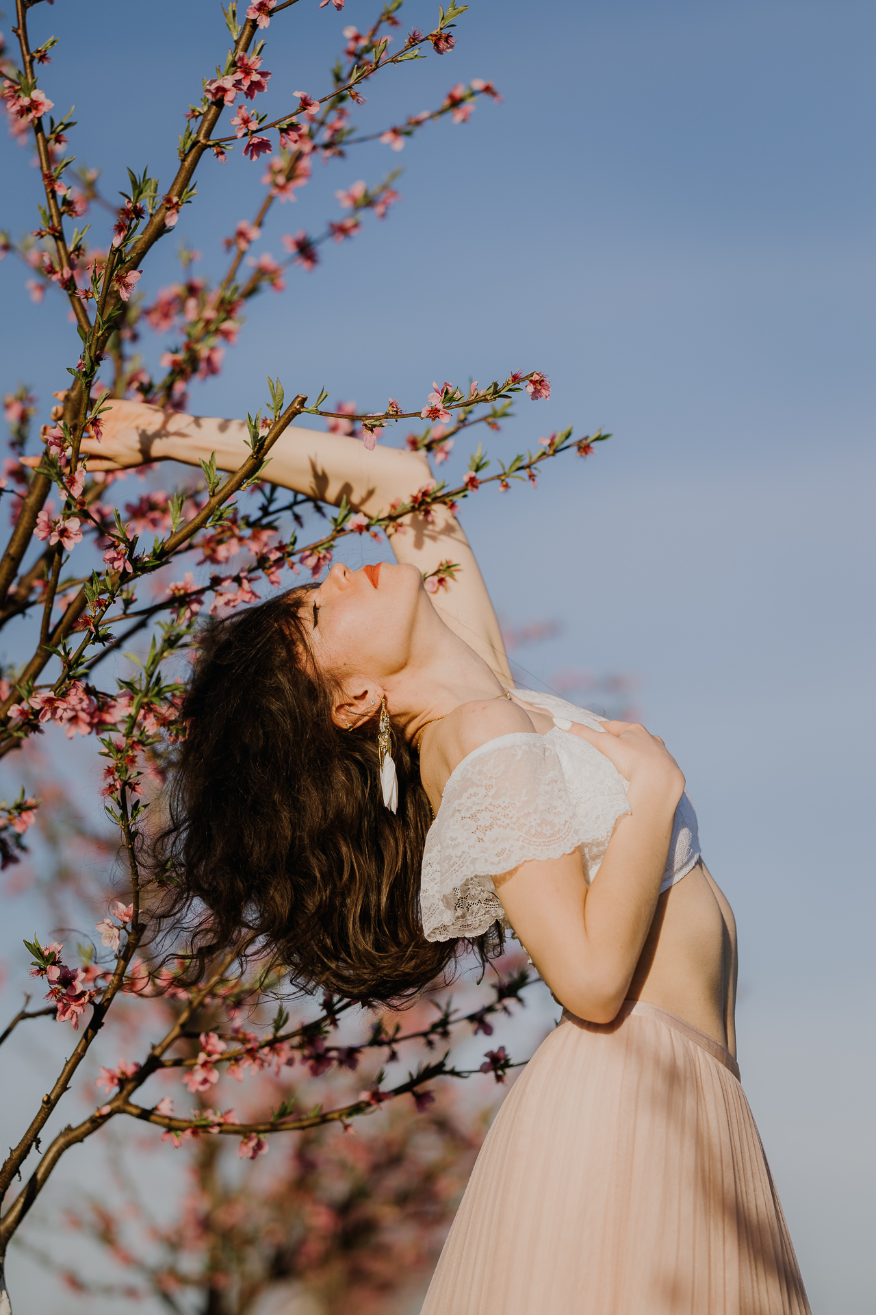 Portret kobiety w kwitnącym sadzie pod Krakowem, modelka na tle brzoskwini w pełnym rozkwicie, wiosenna sesja fotograficzna