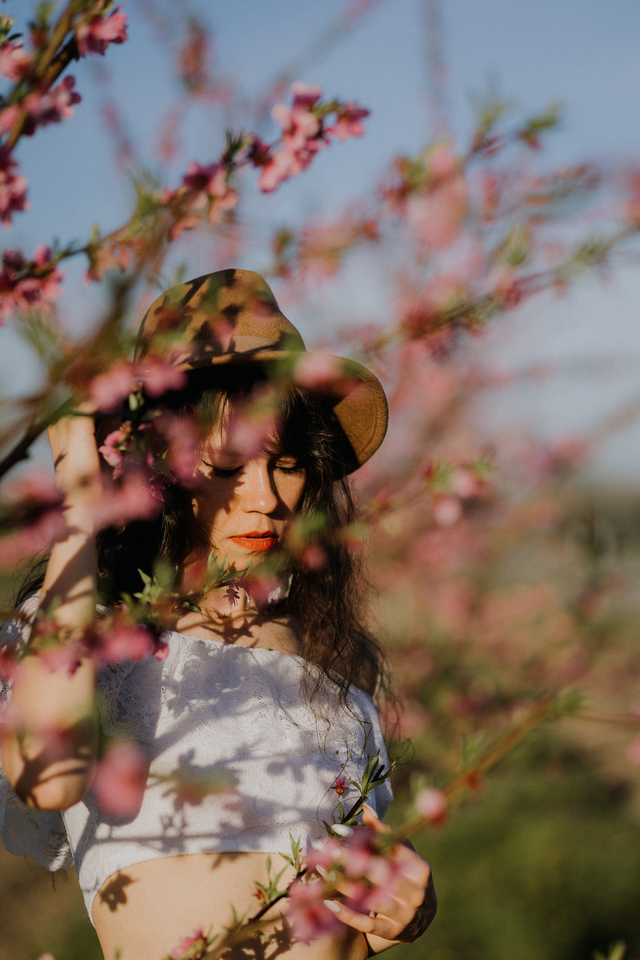 Portret kobiety w kapeluszu w kwitnącym sadzie pod Krakowem, modelka na tle brzoskwini w pełnym rozkwicie, wiosenna sesja fotograficzna