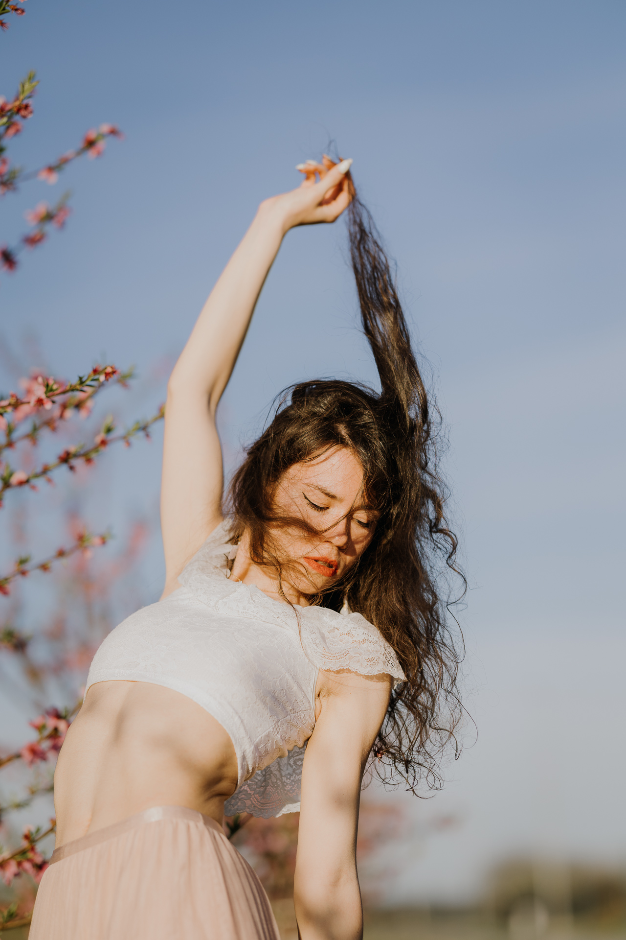 kobieta tańczy w kwitnącym sadzie pod Krakowem, modelka na tle brzoskwini w pełnym rozkwicie, wiosenna sesja fotograficzna