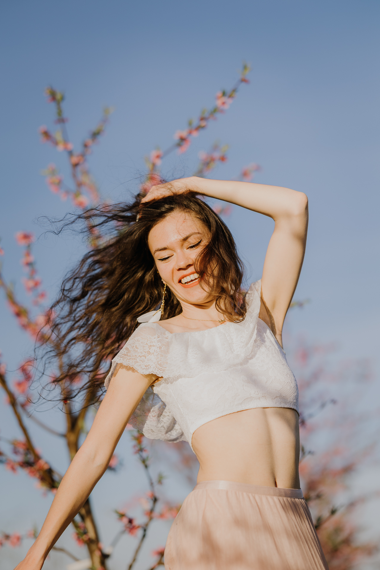 kobieta tańczy w kwitnącym sadzie pod Krakowem, modelka na tle brzoskwini w pełnym rozkwicie, wiosenna sesja fotograficzna