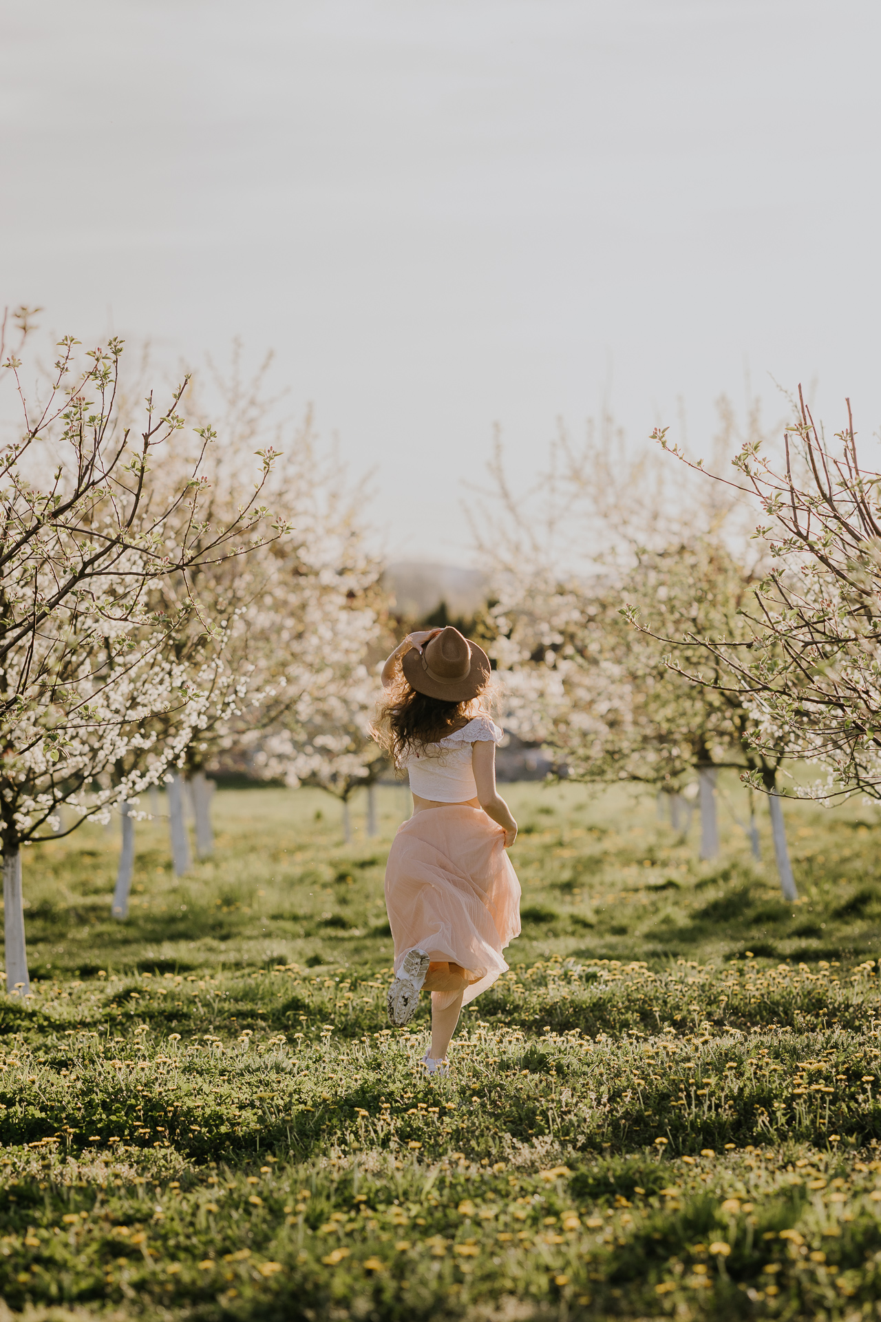 kobieta biegnie w kwitnącym sadzie pod Krakowem, modelka na tle jabłoni w pełnym rozkwicie, wiosenna sesja fotograficzna