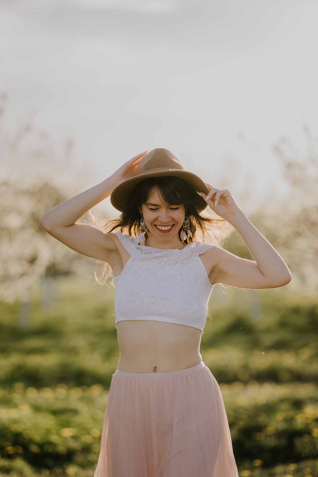 kobieta biegnie trzymając kapelusz w kwitnącym sadzie pod Krakowem, wiosenna sesja fotograficzna