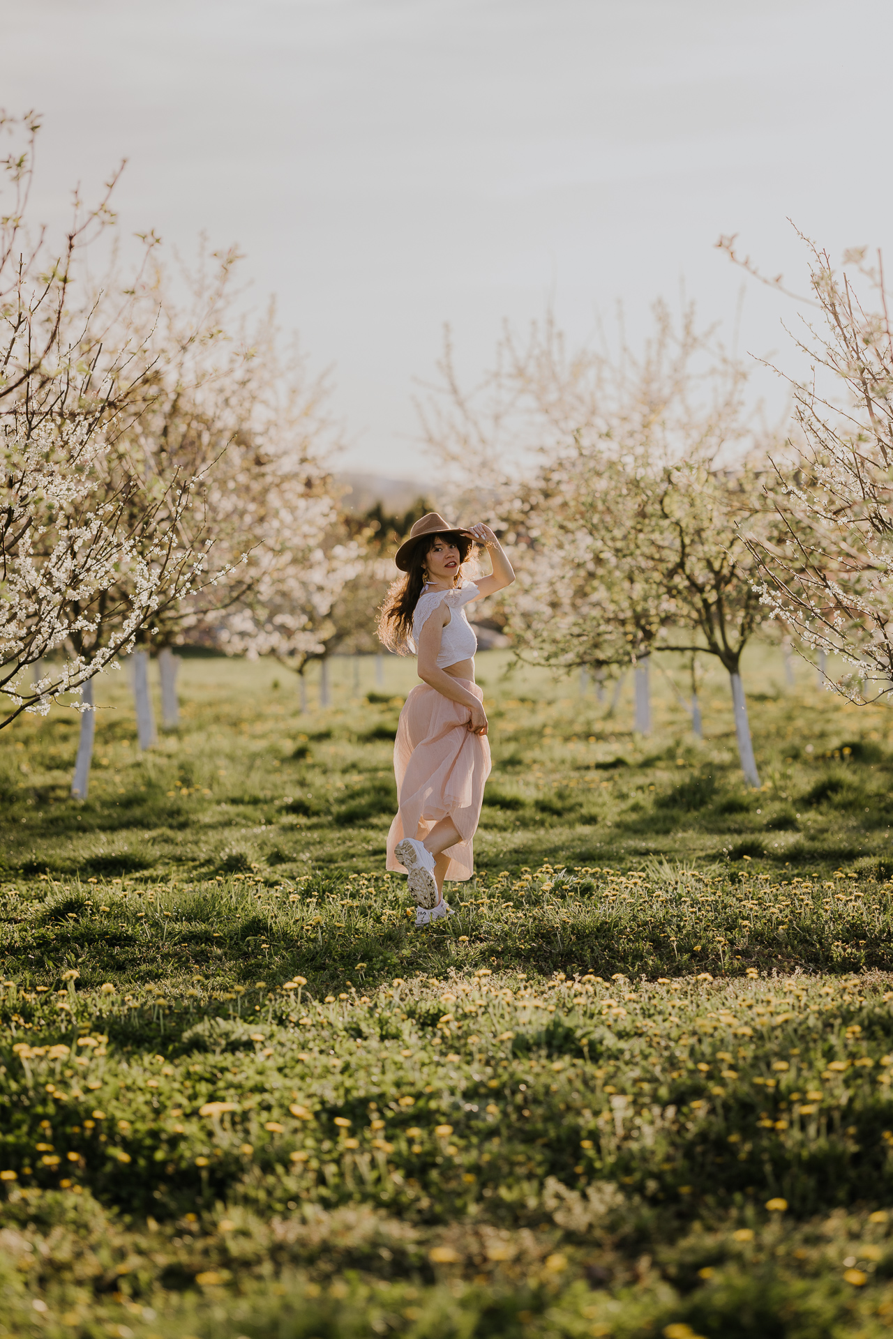 kobieta biegnie trzymając kapelusz w kwitnącym sadzie pod Krakowem, wiosenna sesja fotograficzna