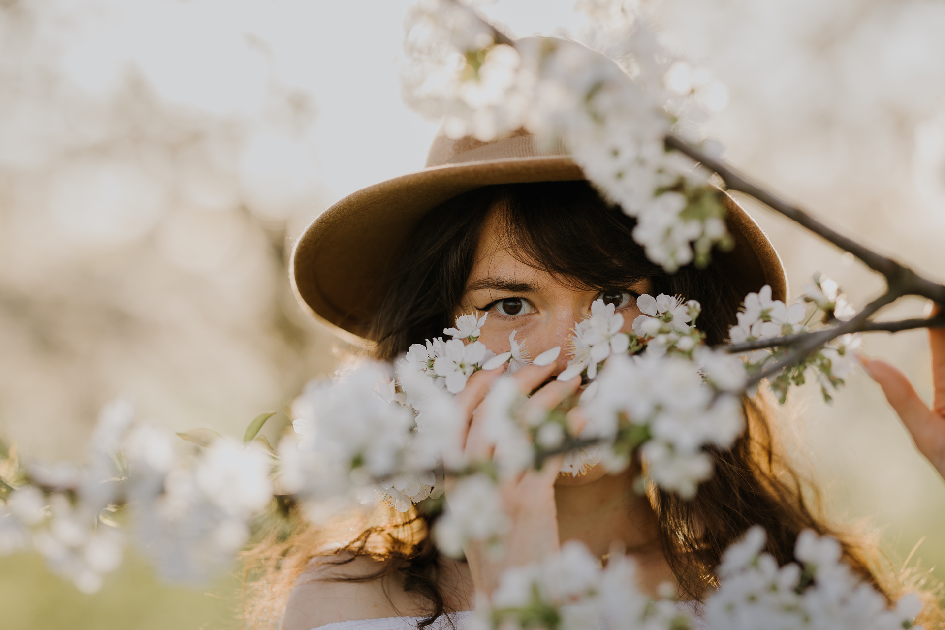 Zbliżenie twarzy modelki podczas sesji w kwitnącym sadzie jabłoniowym, profesjonalna fotografia kobieca, okolice Krakowa