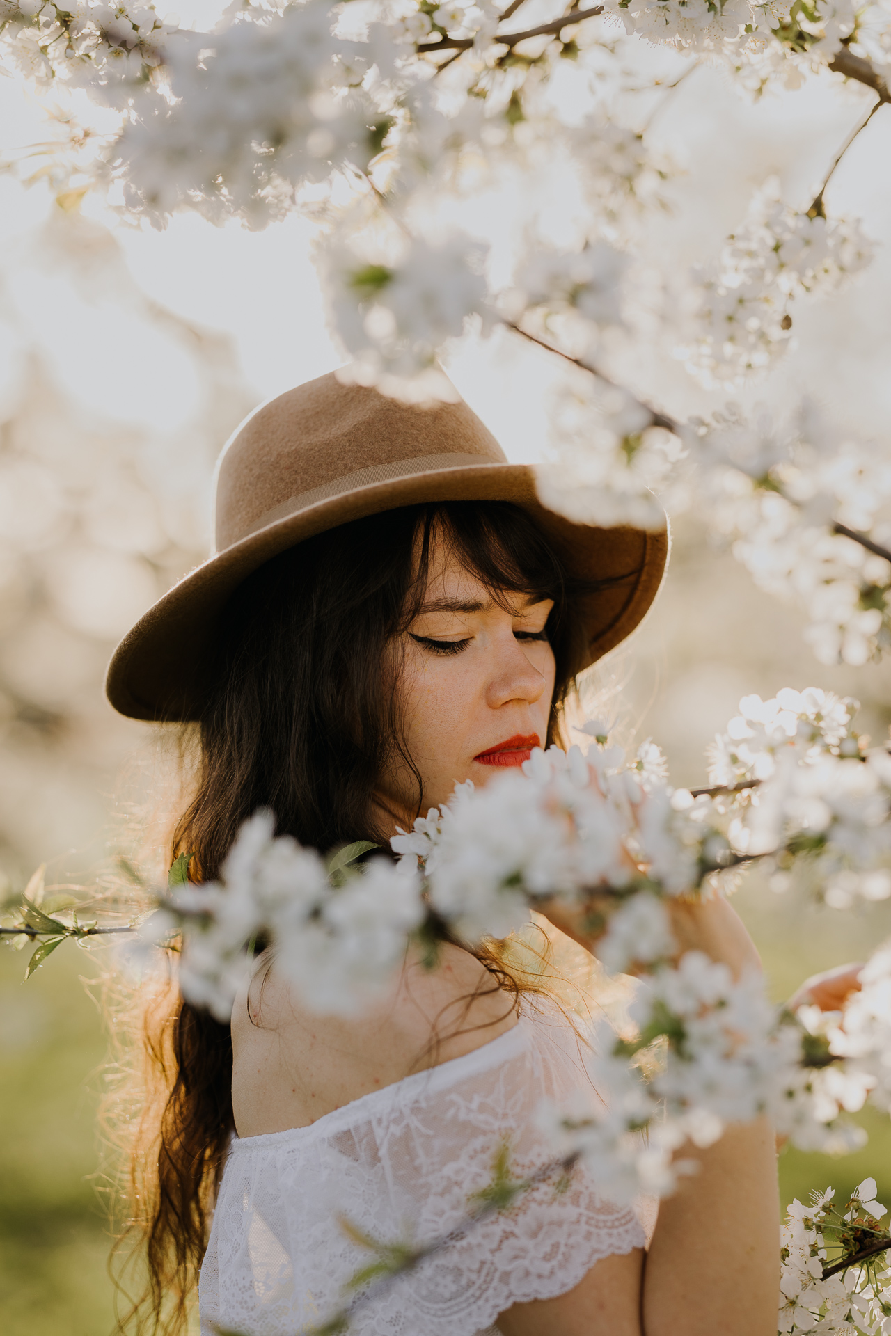 Zbliżenie twarzy modelki podczas sesji w kwitnącym sadzie jabłoniowym, profesjonalna fotografia kobieca, okolice Krakowa