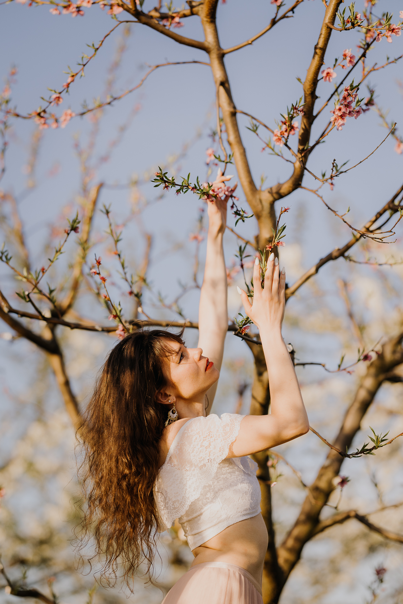 Kobieta przy drzewach owocowych w kwitnącym sadzie, wiosenna sesja kobieca