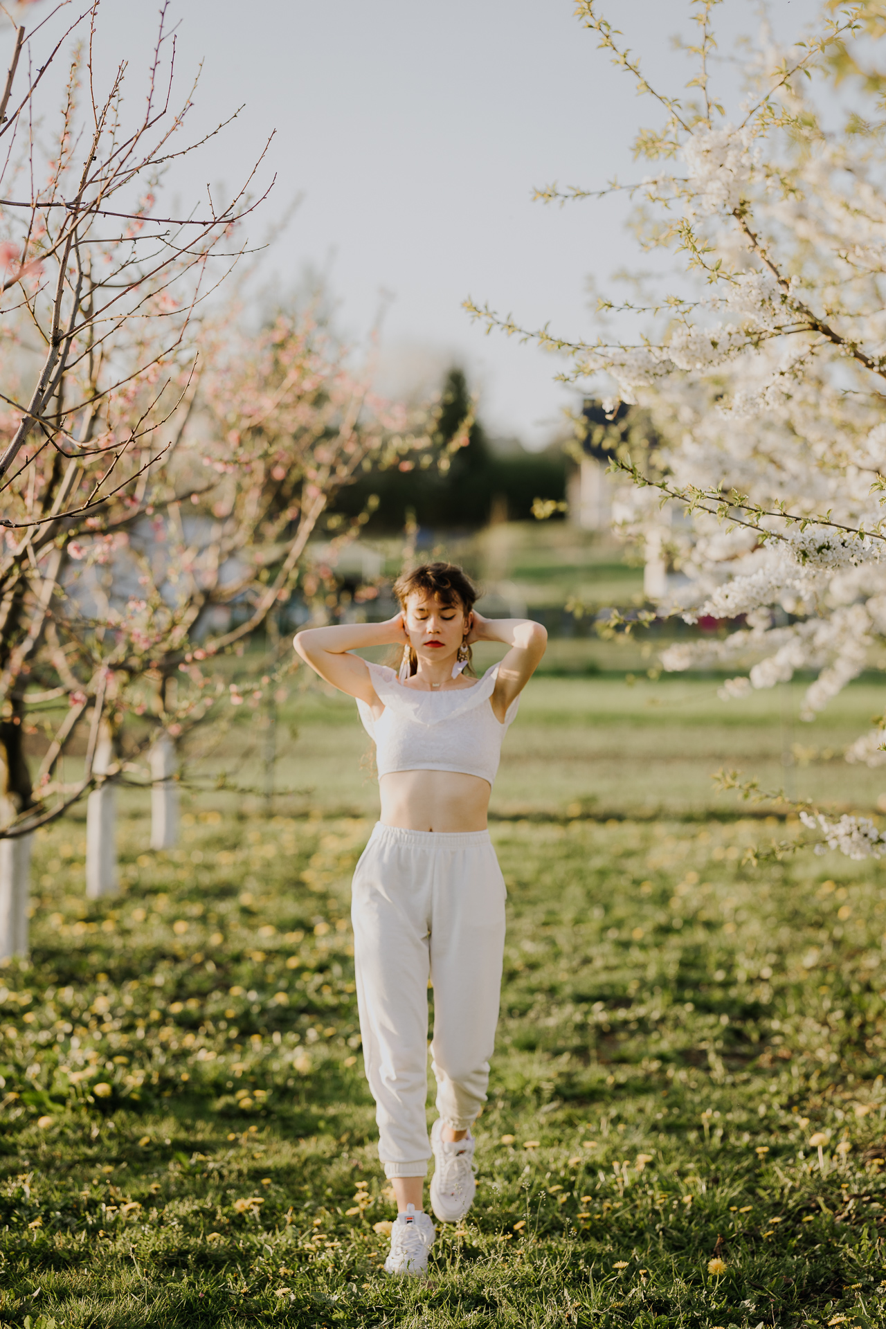 Kobieta w białym ubraniu na tle kwitnących drzew owocowych, sesja fotograficzna wiosenna w sadzie pod Krakowem