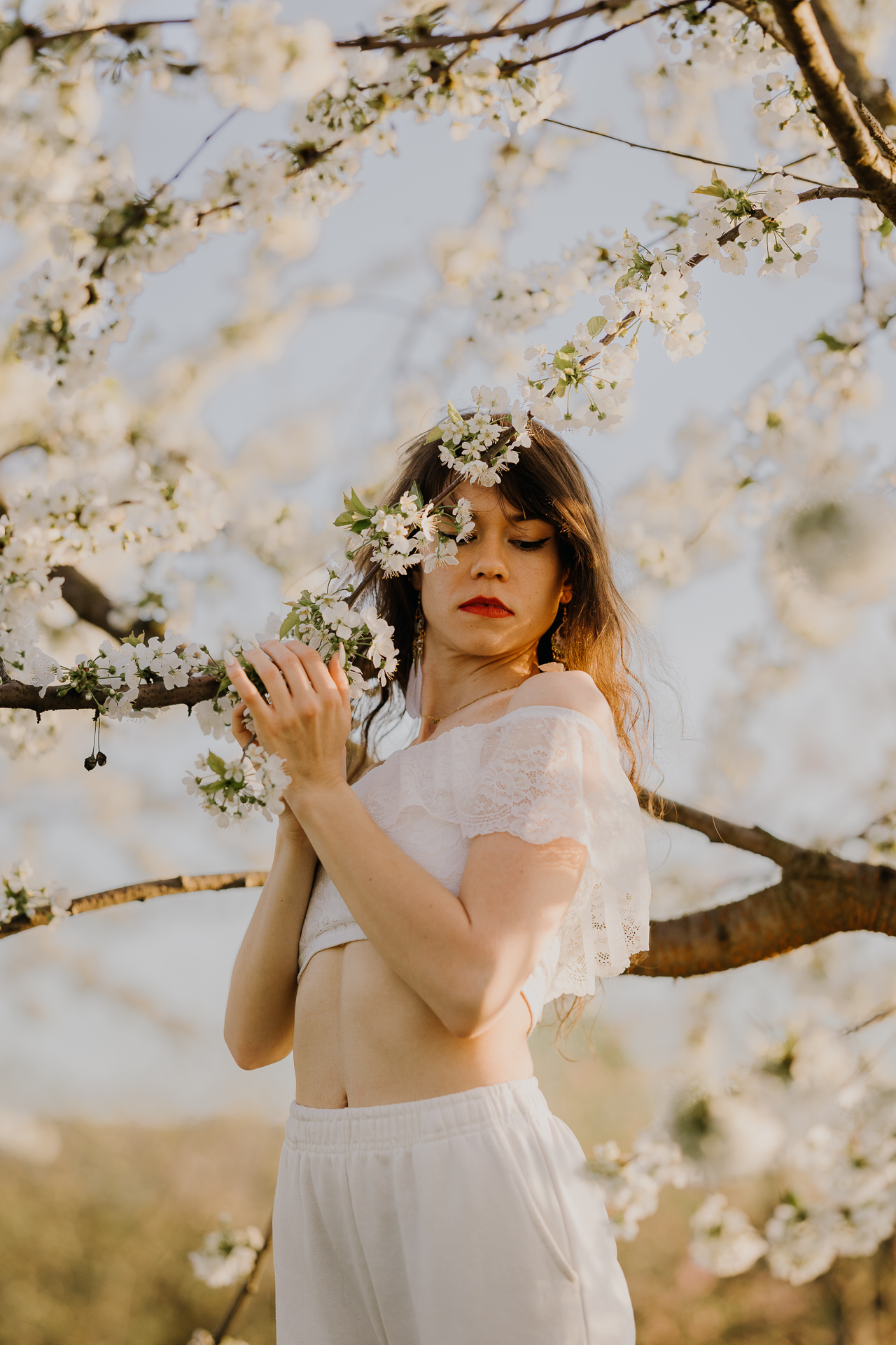 Portret kobiety w białym ubraniu pośród kwitnących drzew owocowych i zachodzącego słońca, sesja fotograficzna wiosenna w sadzie pod Krakowem