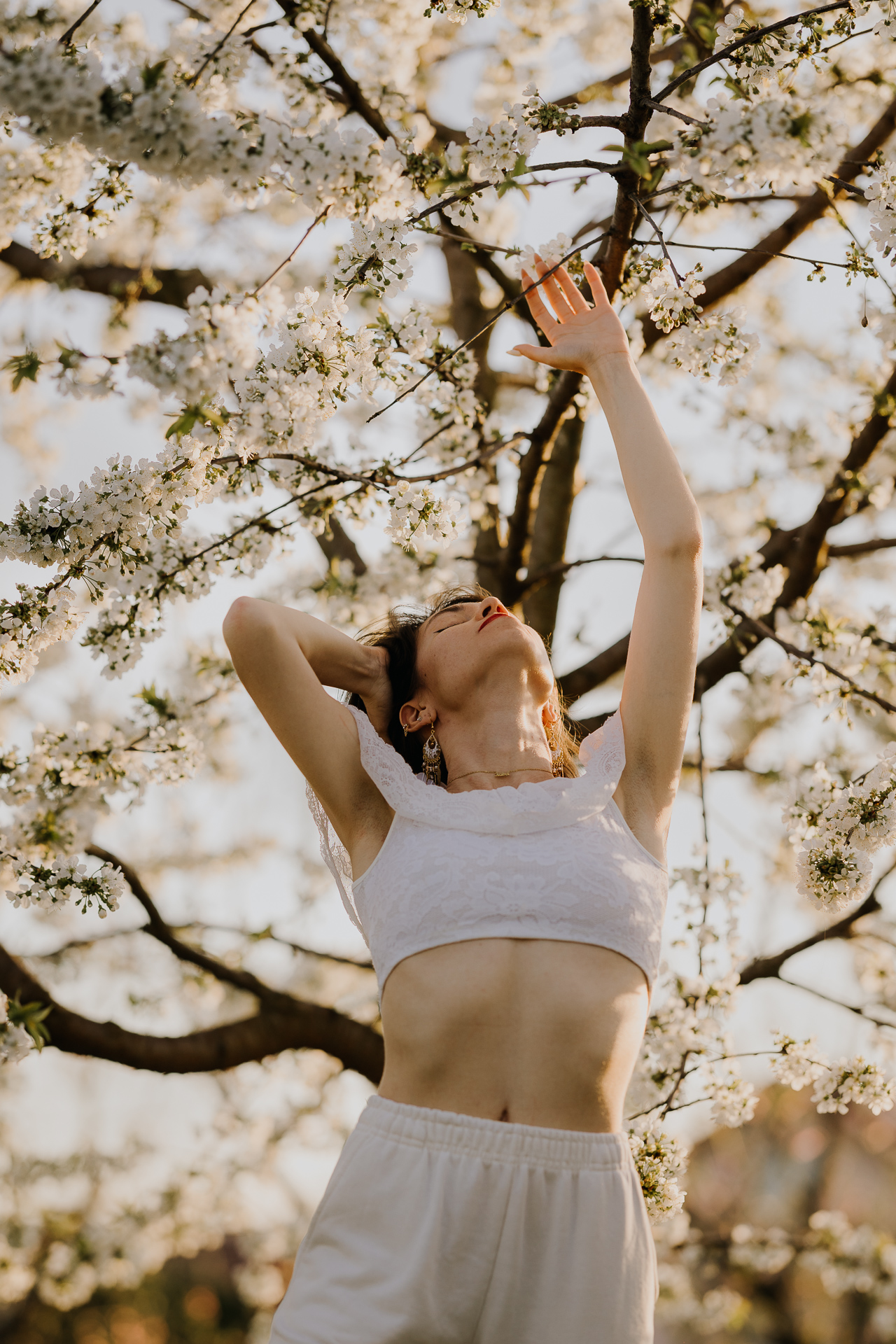 Portret kobiety w białym ubraniu pośród kwitnących drzew owocowych i zachodzącego słońca, sesja fotograficzna wiosenna w sadzie pod Krakowem
