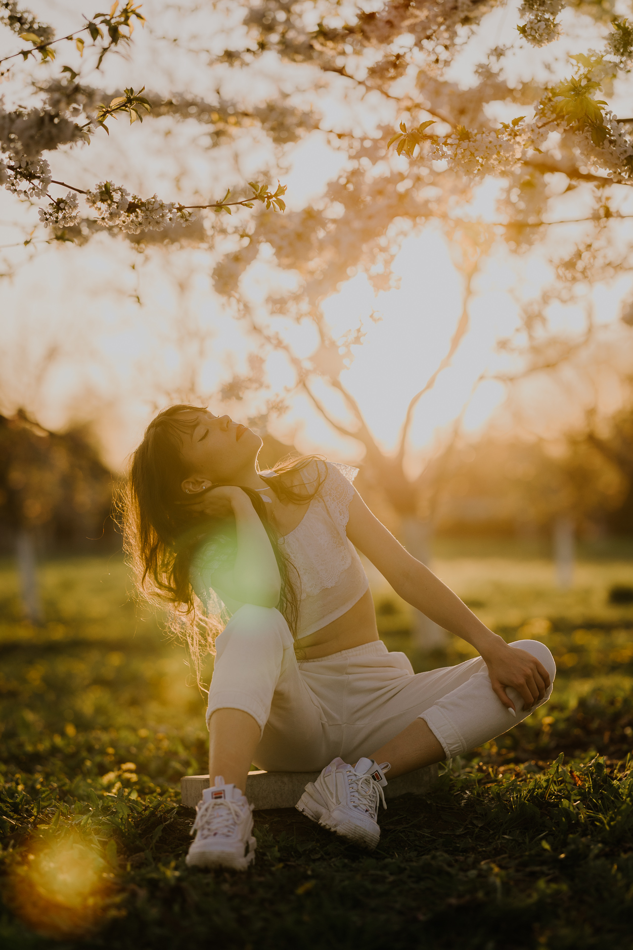 Portret kobiecy w kwitnącym sadzie podczas zachodzącego słońca pod Krakowem, modelka wśród jabłoni w pełnym rozkwicie, wiosenna sesja fotograficzna