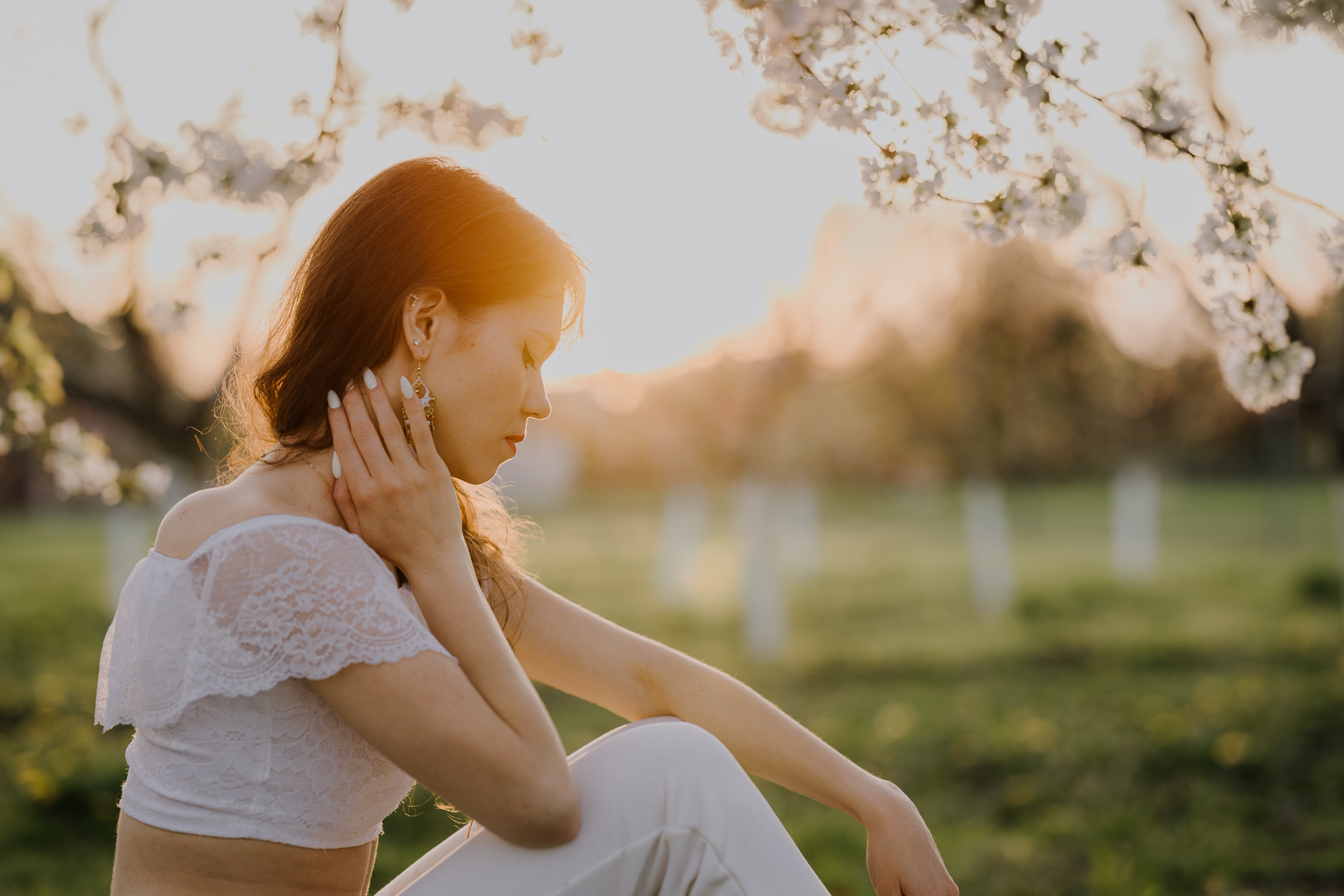 Portret kobiecy w kwitnącym sadzie podczas zachodzącego słońca pod Krakowem, modelka wśród jabłoni w pełnym rozkwicie, wiosenna sesja fotograficzna