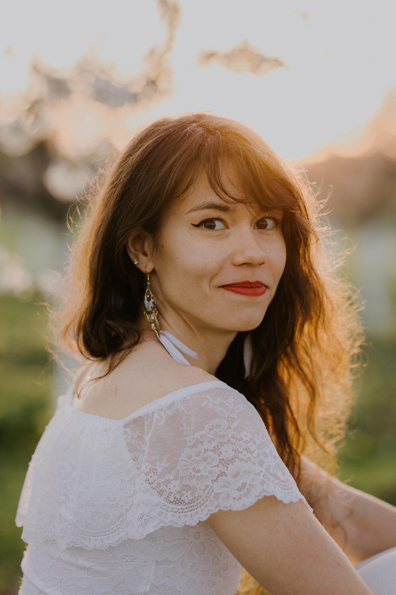 Portret kobiecy w kwitnącym sadzie podczas zachodzącego słońca pod Krakowem, modelka wśród jabłoni w pełnym rozkwicie, wiosenna sesja fotograficzna