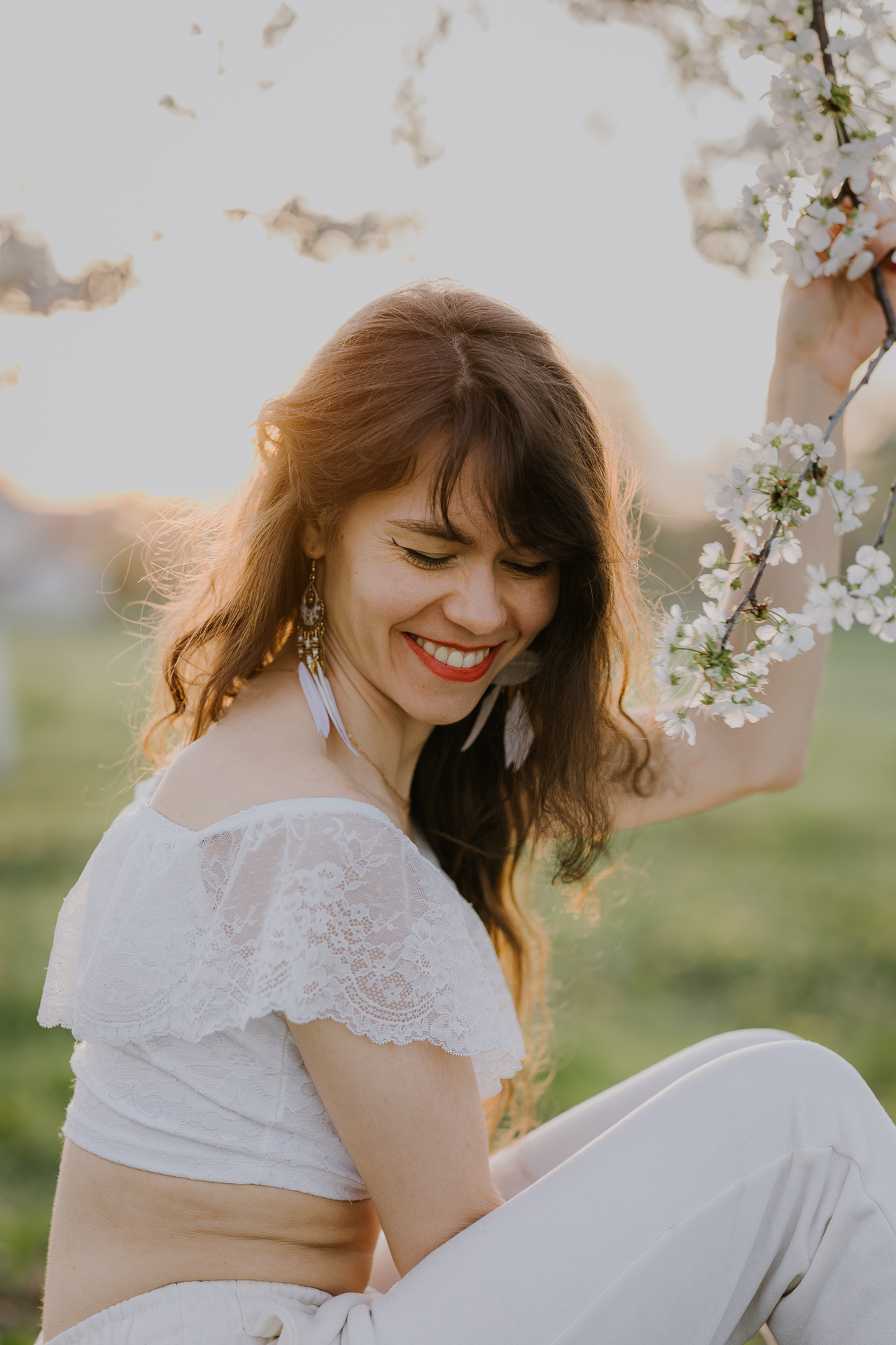 Portret kobiecy w kwitnącym sadzie podczas zachodzącego słońca pod Krakowem, modelka wśród jabłoni w pełnym rozkwicie, wiosenna sesja fotograficzna