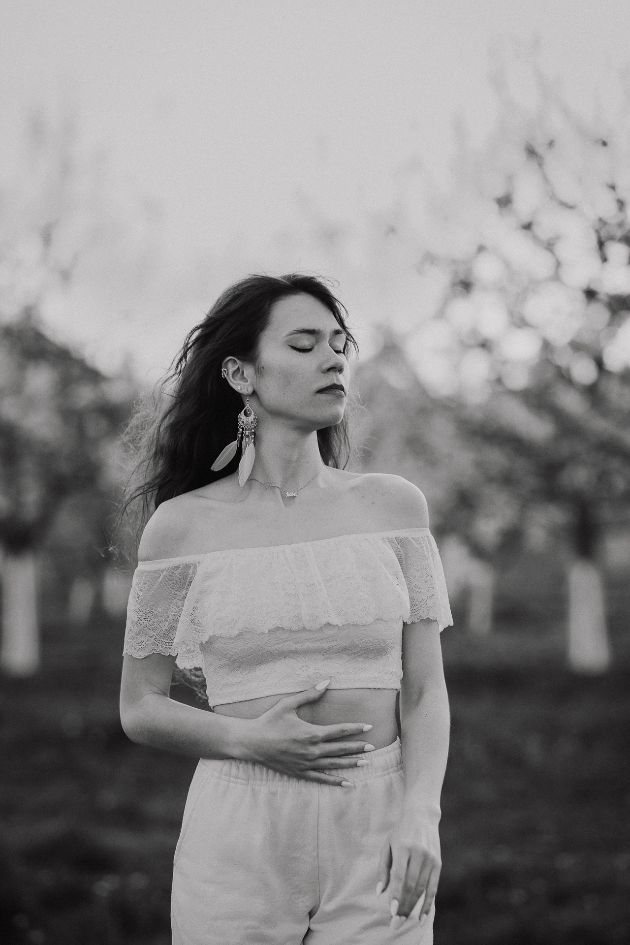 Kobieta w białej bluzce i spodniach na tle kwitnących drzew owocowych, sesja fotograficzna wiosenna w sadzie pod Krakowem