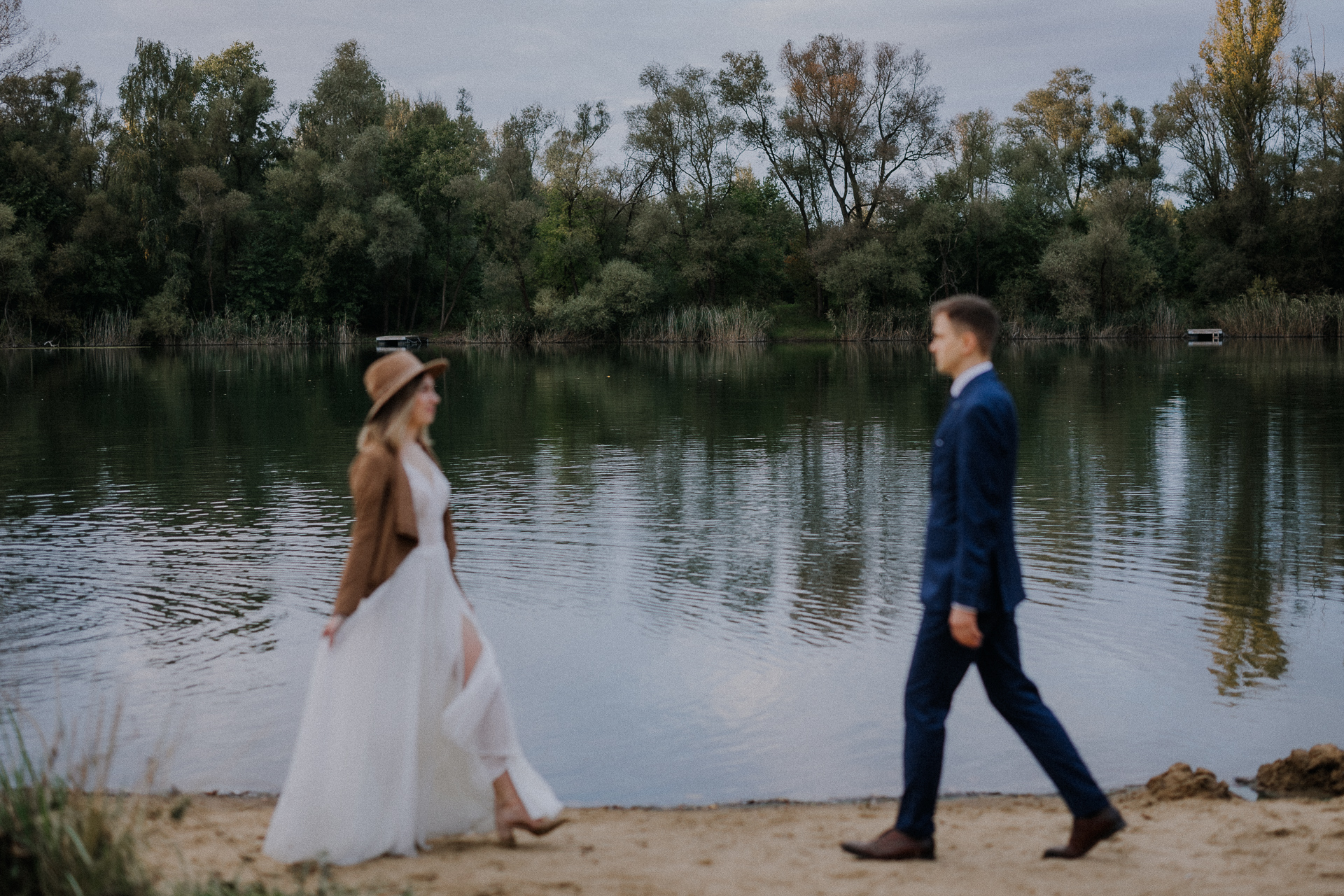 Państwo młodzi idą do siebie na tle jeziora