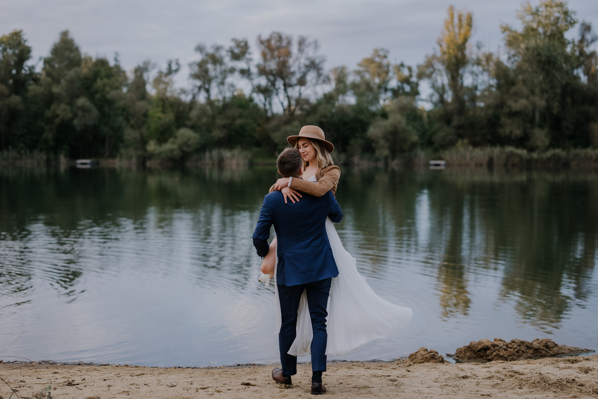 pan młody podnosi pannę młodą na tle stawu