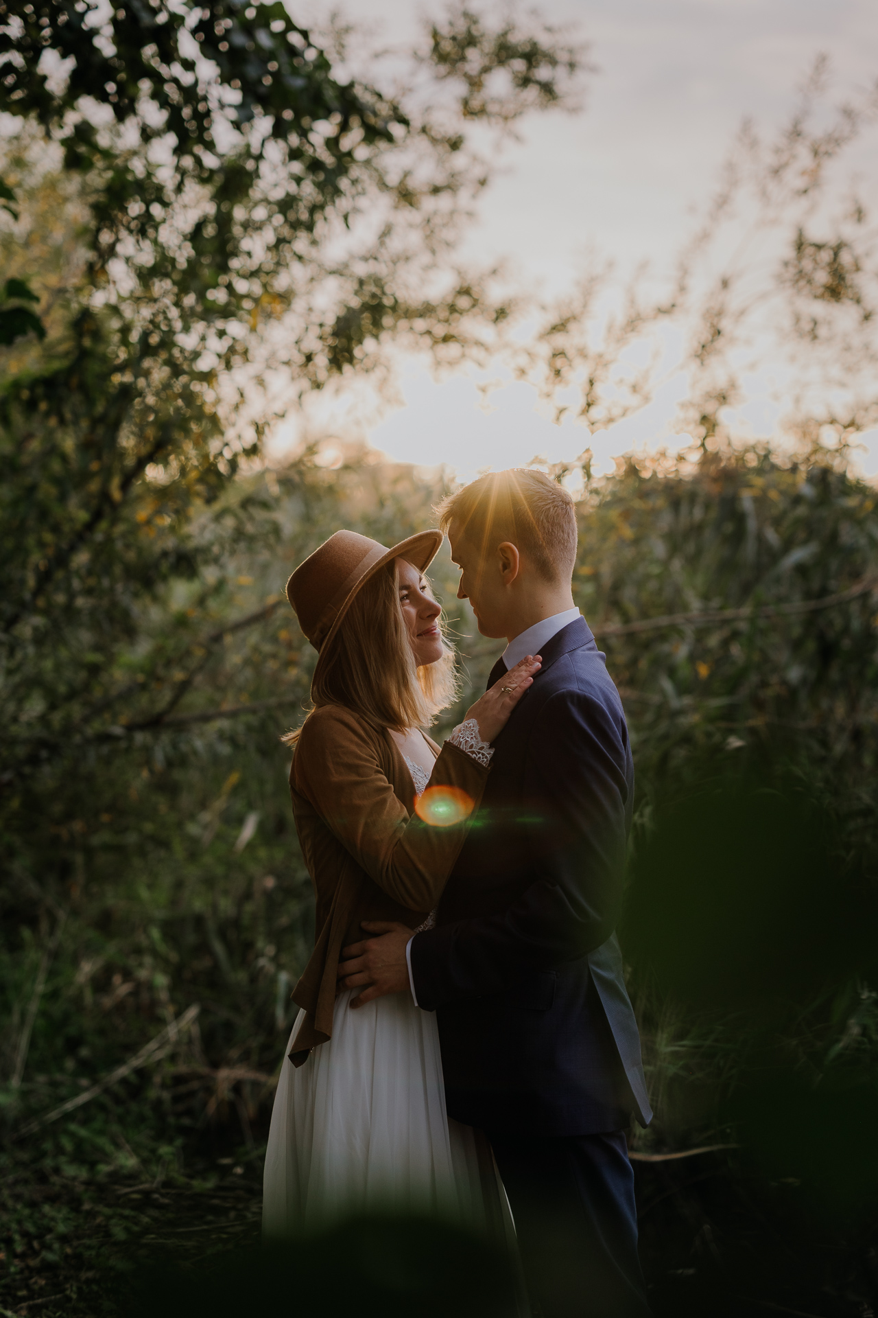 państwo młodzi przytulają się na tle zachodzącego słońca