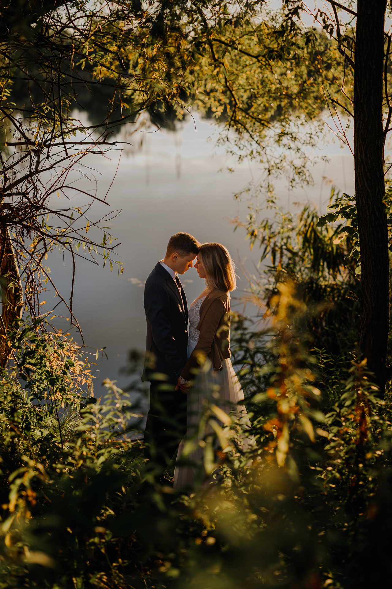 państwo młodzi przytulają się na tle zachodzącego słońca