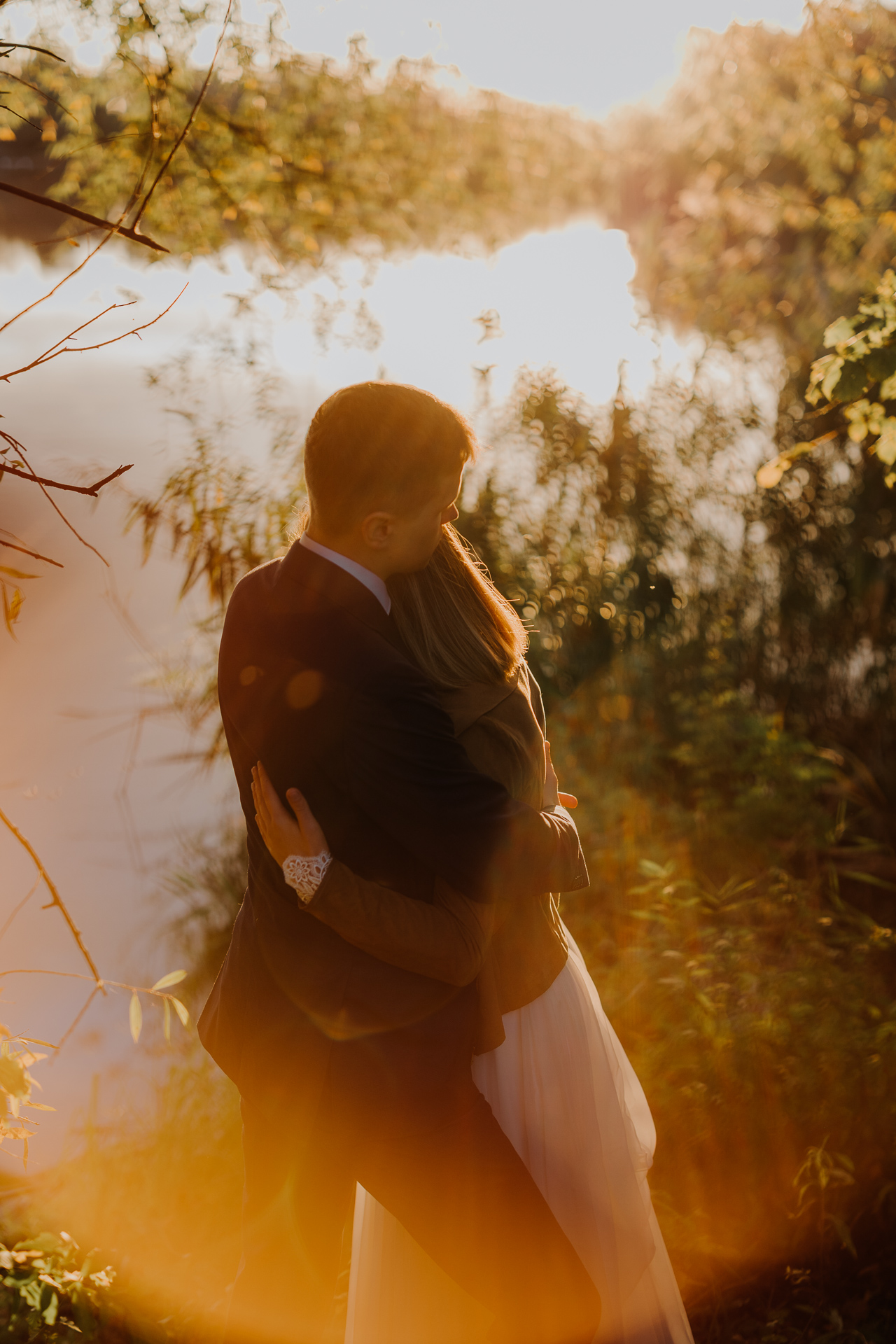 państwo młodzi przytulają się na tle zachodzącego słońca