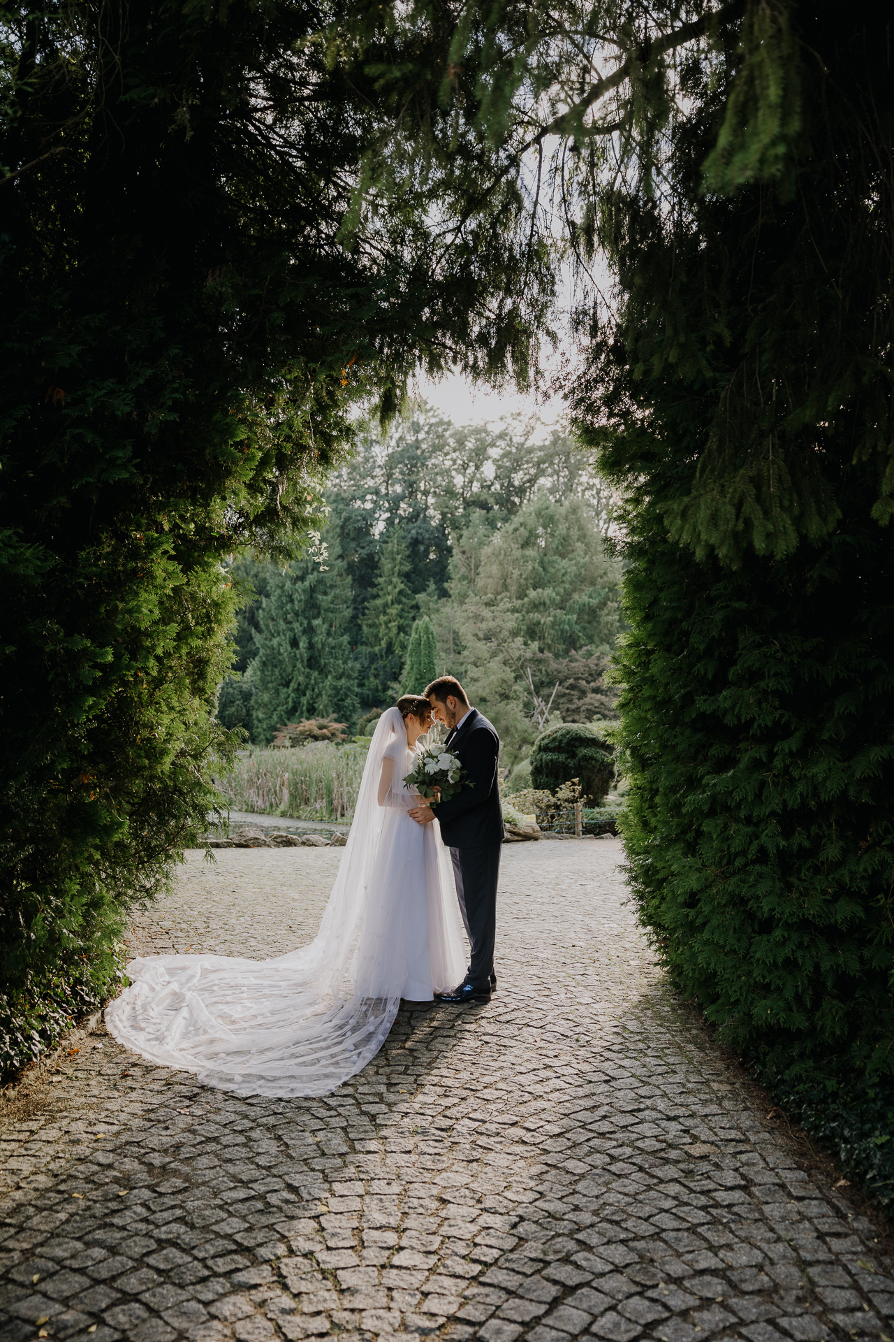 Nowożeńcy przytuleni pod drzewami w arboretum Bolestraszyce, plenerowa sesja poślubna, profesjonalna fotografia ślubna