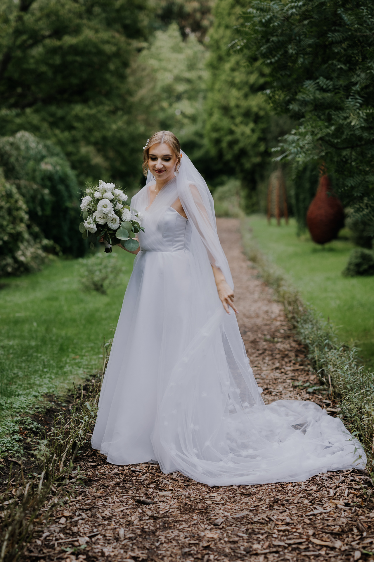 Portret panny młodej w białej sukni ślubnej pośród kwiatów Arboretum Bolestraszyce, romantyczna fotografia ślubna, okolice Przemyśla
