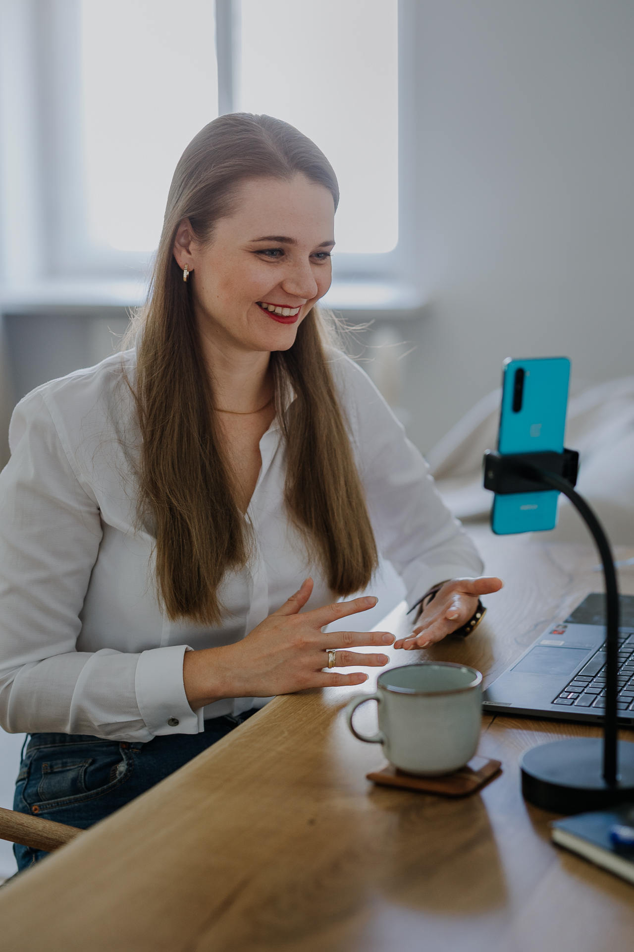 kobieta stoi i uśmiecha się do telefonu, gestykulując przy tym dłońmi podczas sesji wizerunkowej w studio w Krakowie