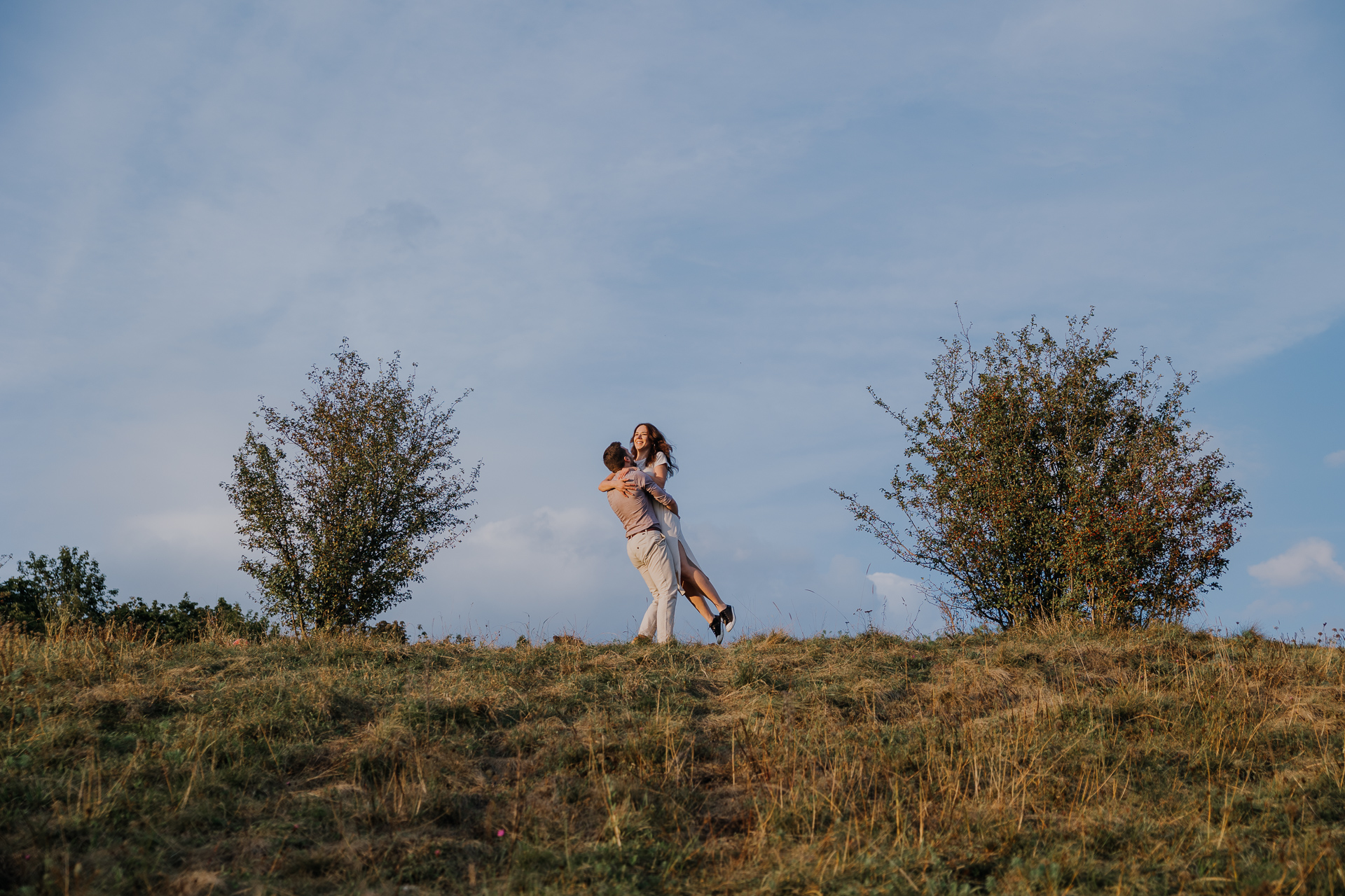chłopak podnosi dziewczynę na tle niebieskiego nieba
