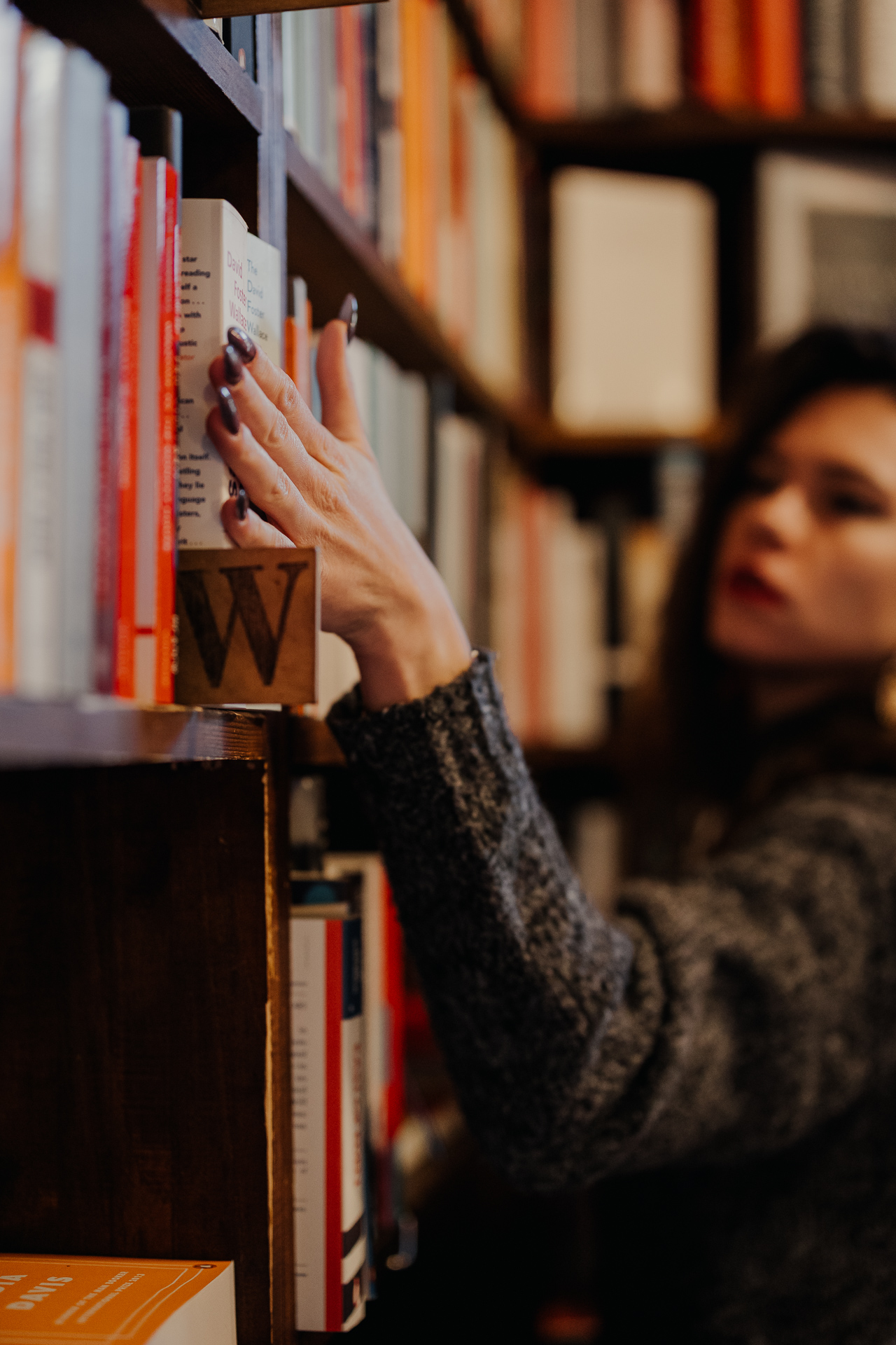 kobieta przesuwa ręką po regale z książkami