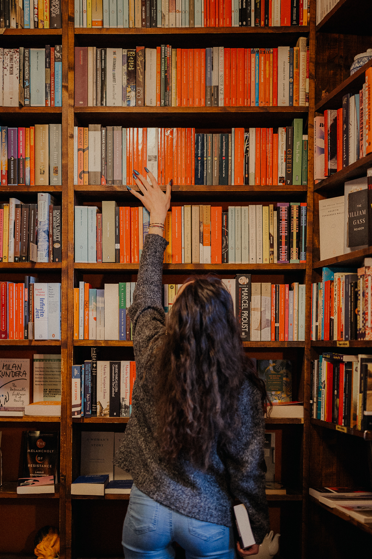 kobieta przesuwa ręką po regale z książkami