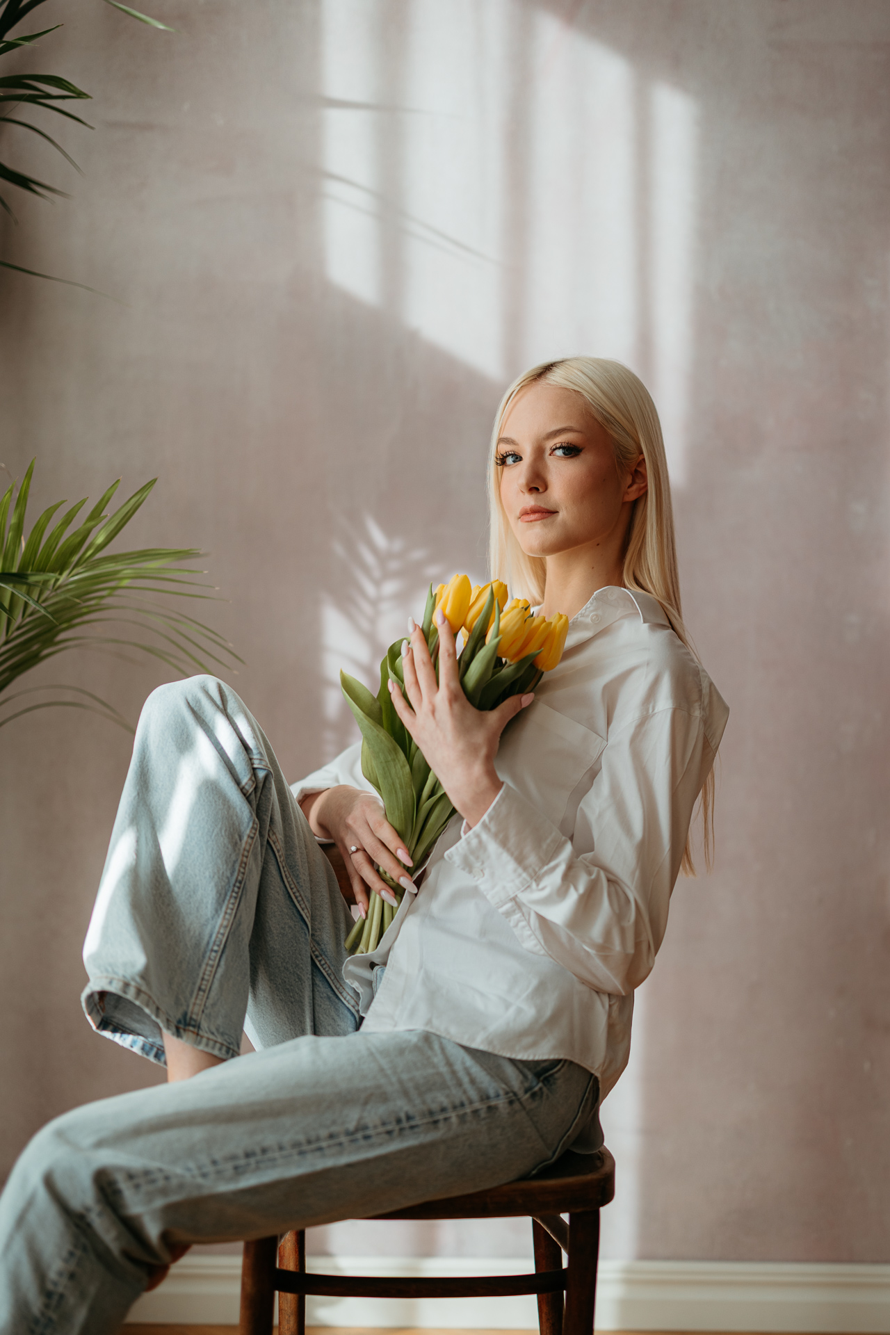 Portret kobiety siedzącej na krześle z żółtymi tulipanami w rękach, miękkie światło wpadające przez okno tworzy wiosenną atmosferę sesji