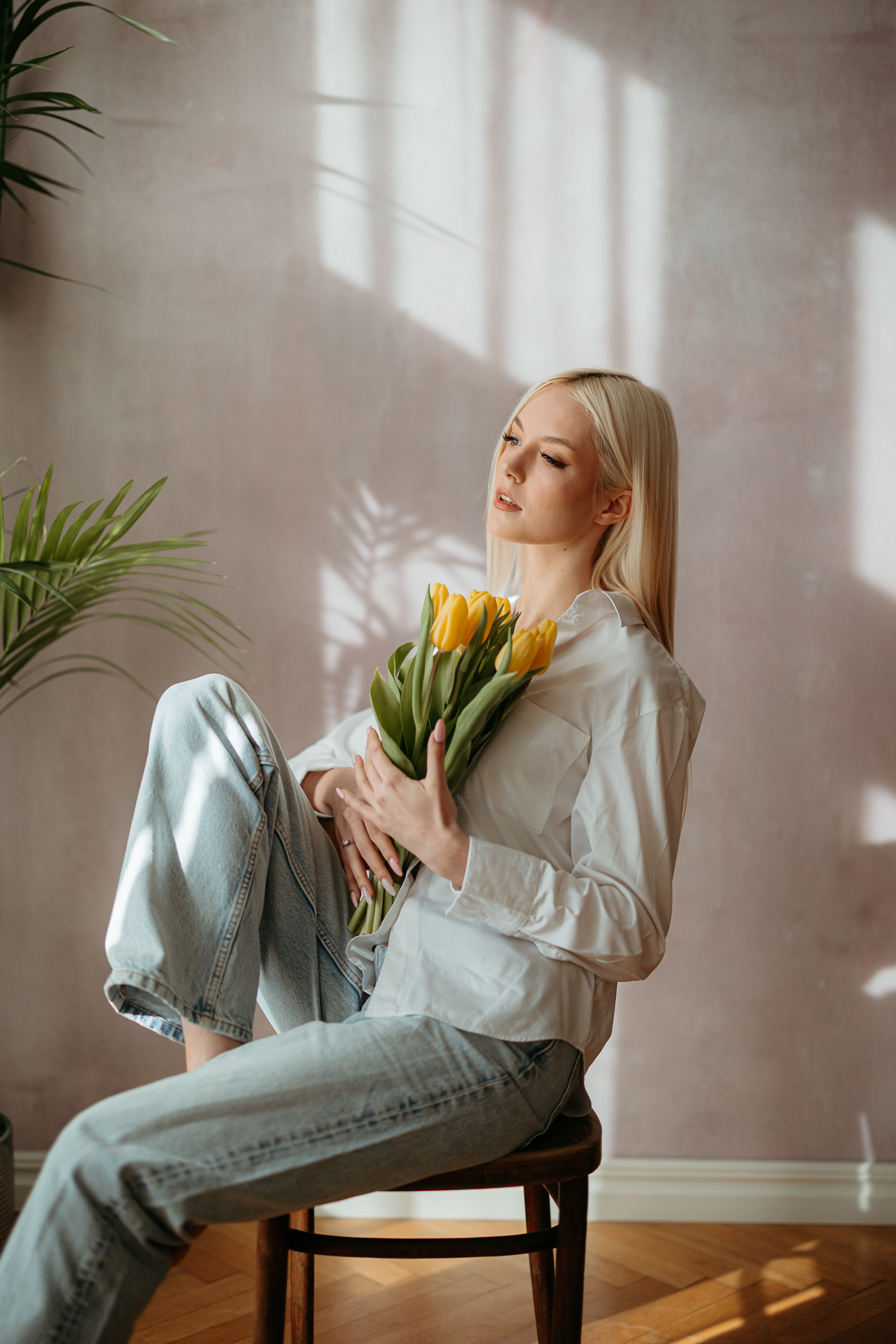 Portret kobiety siedzącej na krześle z żółtymi tulipanami w rękach, miękkie światło wpadające przez okno tworzy wiosenną atmosferę sesji