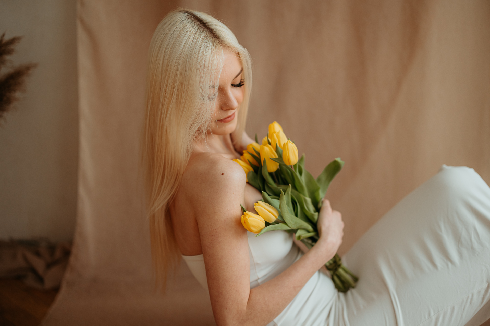 Kobieta siedząca na podłodze z bukietem tulipanów, naturalne światło z okna tworzy subtelny kontur sylwetki w krakowskim studiu