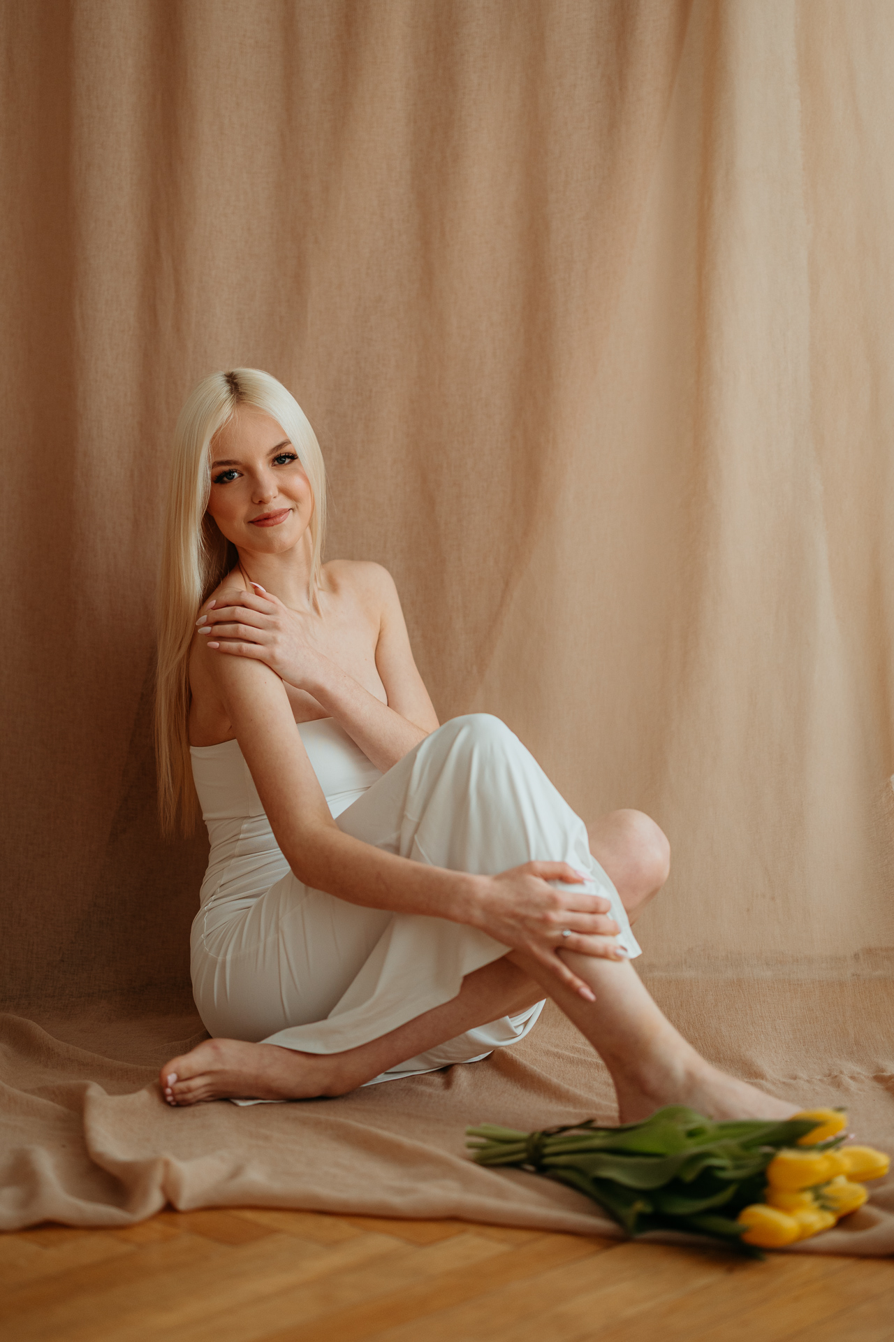 Kobieta siedząca na podłodze z bukietem tulipanów, naturalne światło z okna tworzy subtelny kontur sylwetki w krakowskim studiu