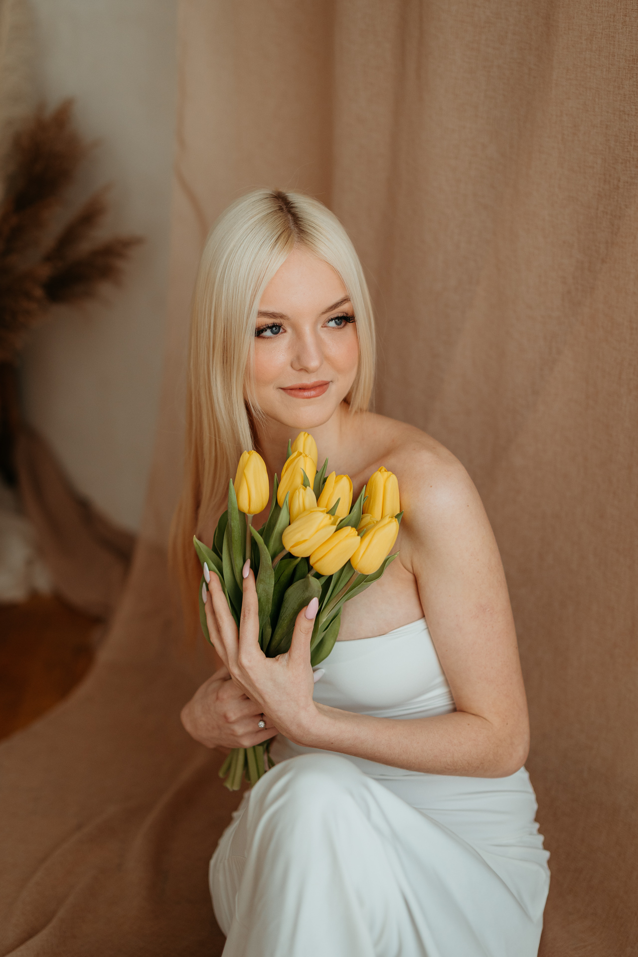 Kobieta siedząca na podłodze z bukietem tulipanów, naturalne światło z okna tworzy subtelny kontur sylwetki w krakowskim studiu