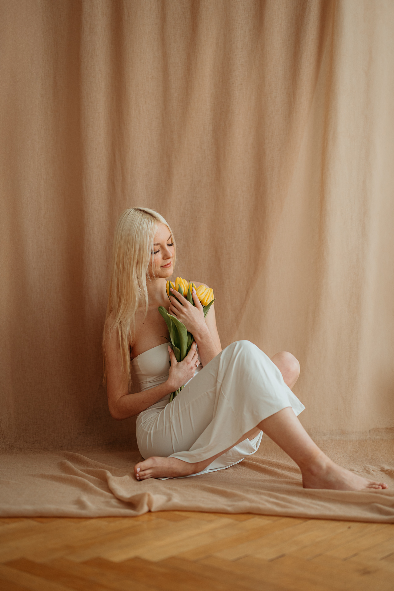 Kobieta siedząca na podłodze z bukietem tulipanów, naturalne światło z okna tworzy subtelny kontur sylwetki w krakowskim studiu