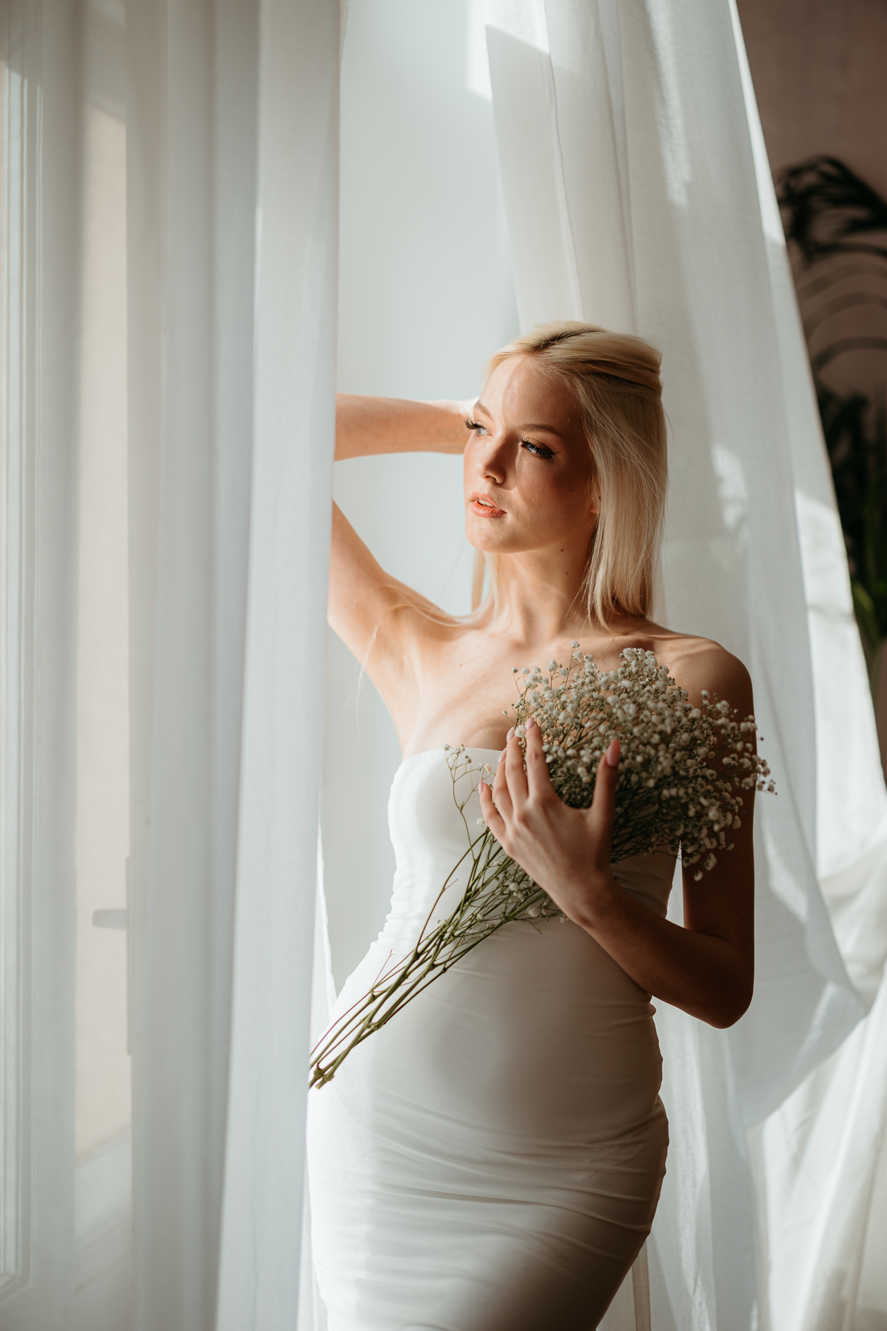 Kreatywne ujęcie kobiety stojącej przy oknie z bukietem gipsówki, Atelier Basztowa