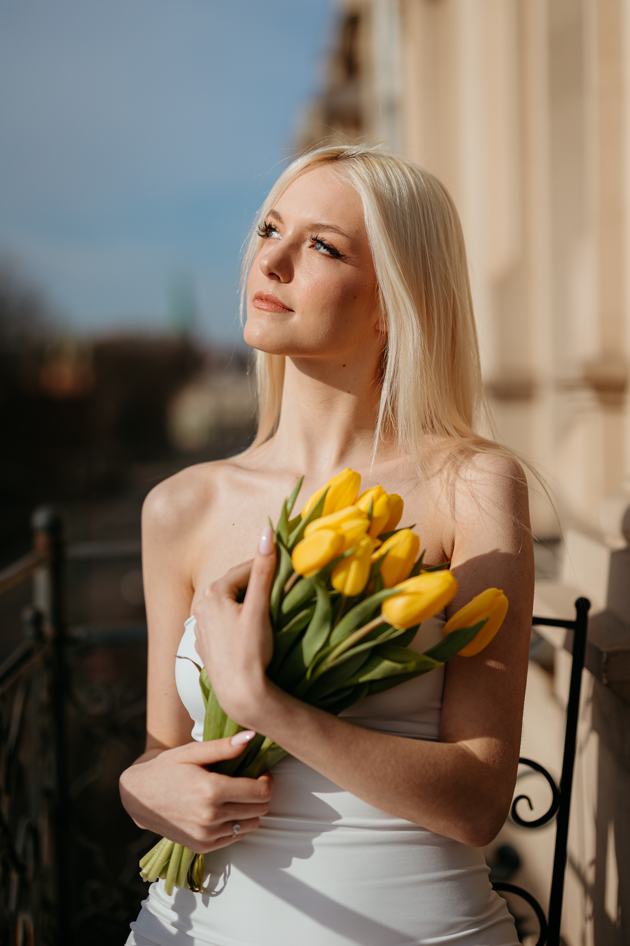 Modelka na balkonie studia fotograficznego trzymająca bukiet żółtych tulipanów, wiosenne światło podkreśla naturalność ujęcia w miejskiej scenerii Krakowa