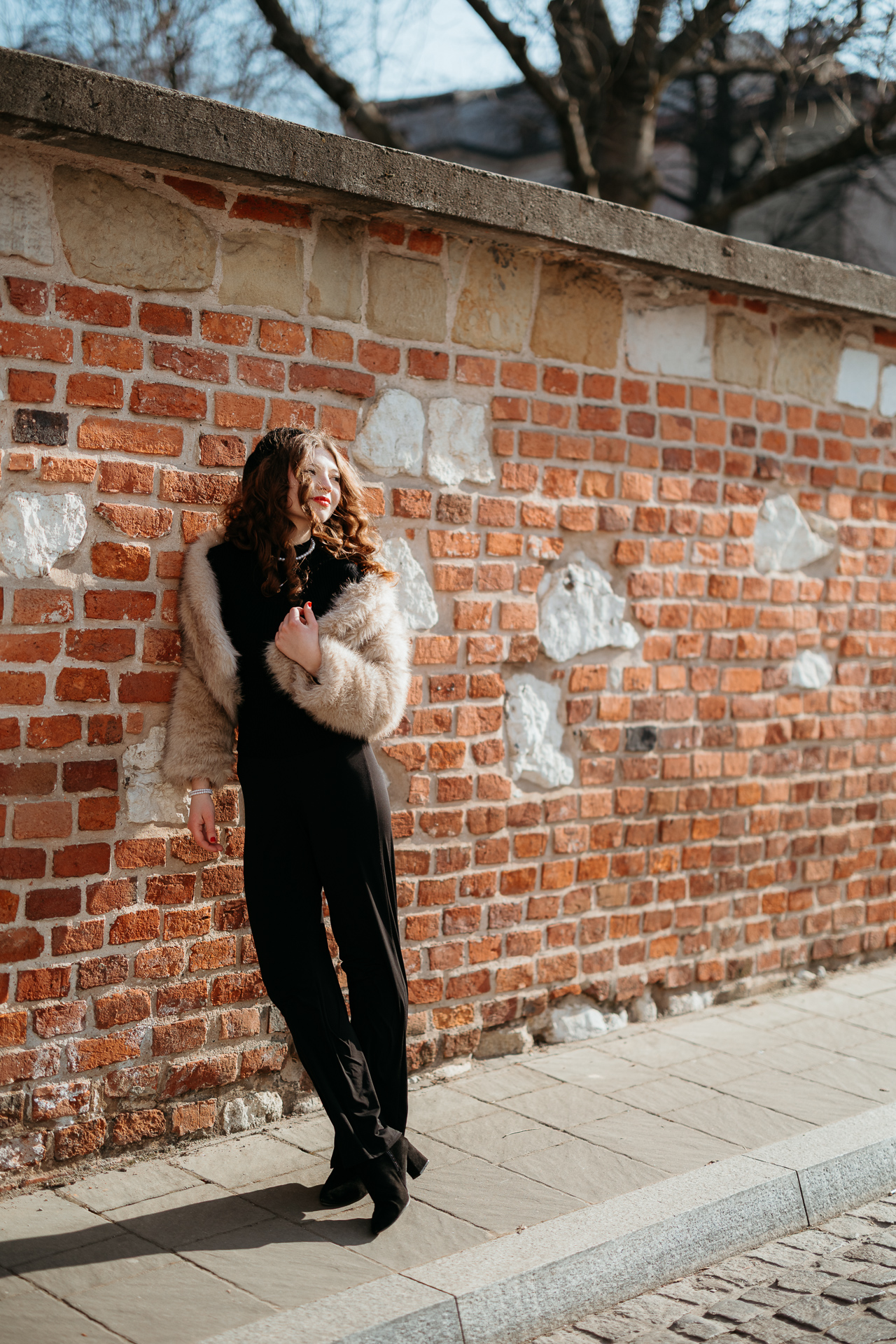 Sesja miejska_Wiktoria-16 Kobieta w stylu paryskim pozuje nonszalancko przy ceglastej ścianie, jej elegancka stylizacja podkreśla kontrast między francuskim szykiem a surowym charakterem miejsca