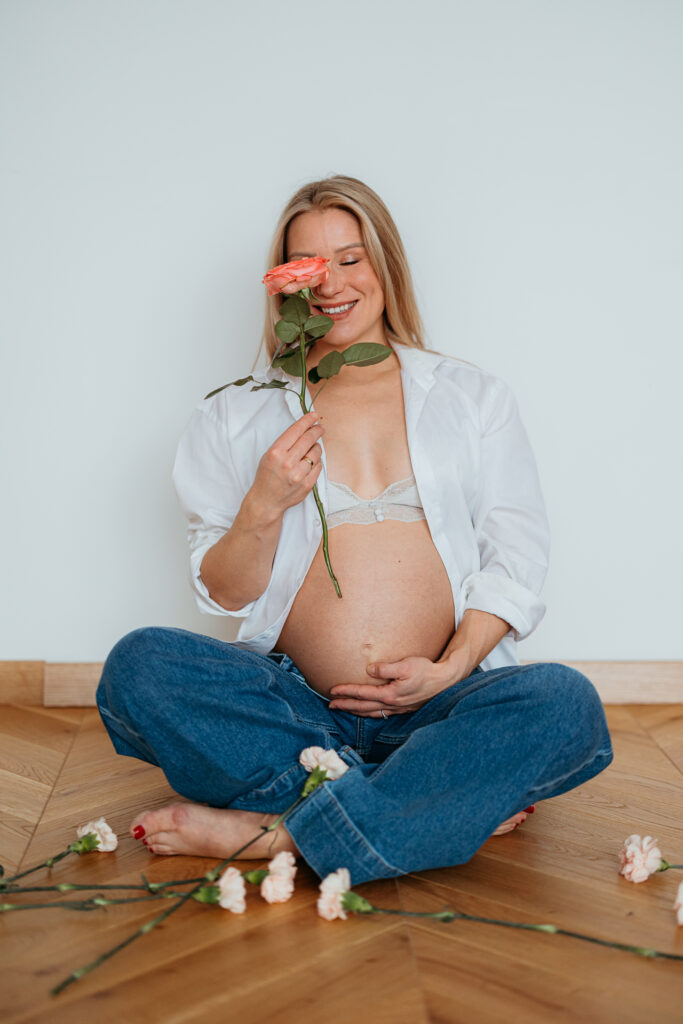 sesja ciazowa, uśmiechnięta przyszła Mama z kwiatem przy twarzy w domu i z odkrytym brzuszkiem w Krakowie