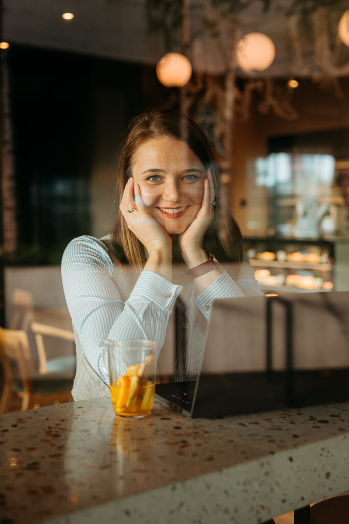uśmiechnięta kobieta - zdjęcie robione przez szybę - sesja wizerunkowa w kawiarni