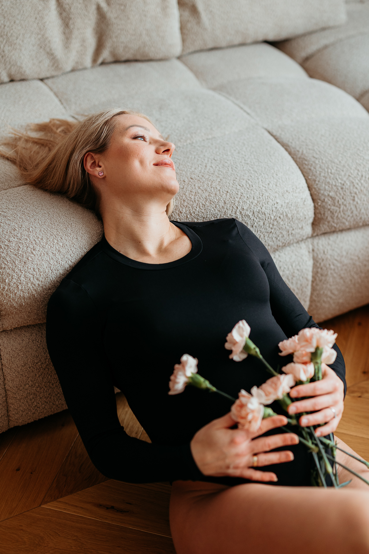 Kobieta w ciąży leży oparta o sofę z kwiatami na brzuchu u siebie w domu, Kraków