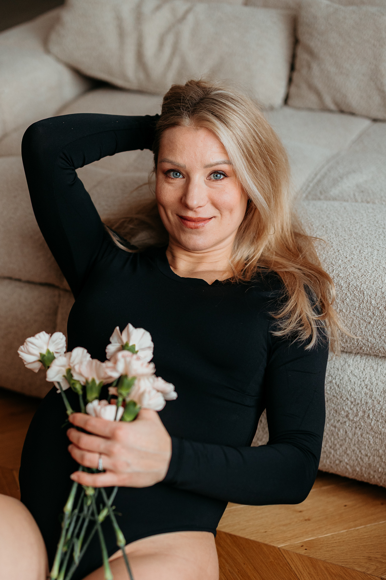 Kobieta w ciąży leży oparta o sofę z kwiatami na brzuchu u siebie w domu, Kraków