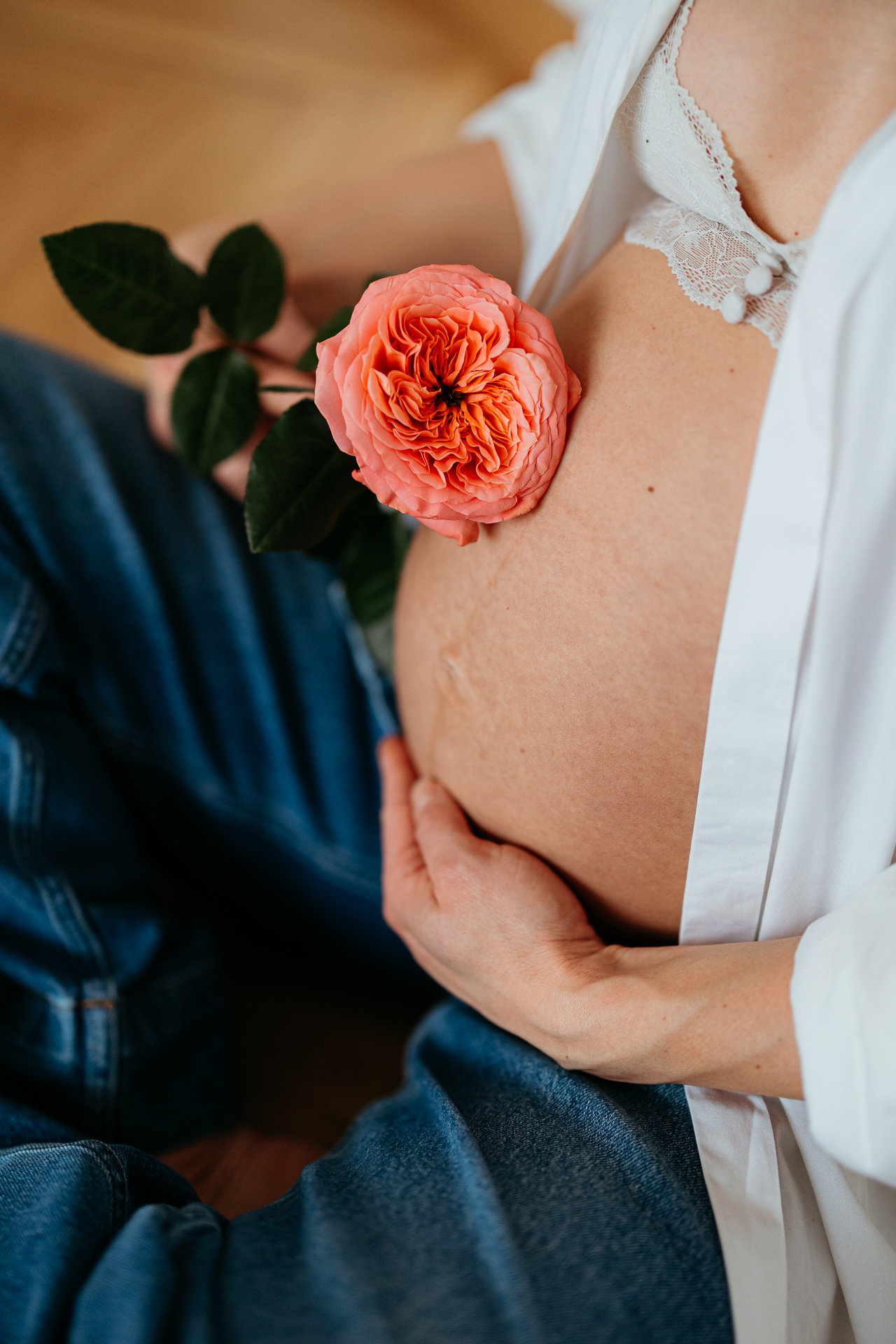 kobieta z odsłoniętym brzuszkiem ciążowym siedzi na podłodze i trzyma różę na brzuszku w domu w Krakowie