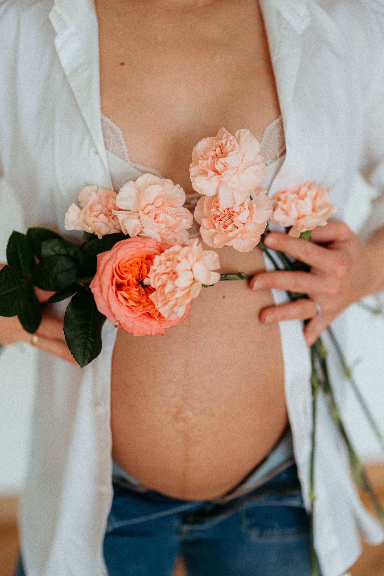 kobieta z odsłoniętym brzuszkiem ciążowym siedzi na podłodze i trzyma róże na brzuszku w domu w Krakowie