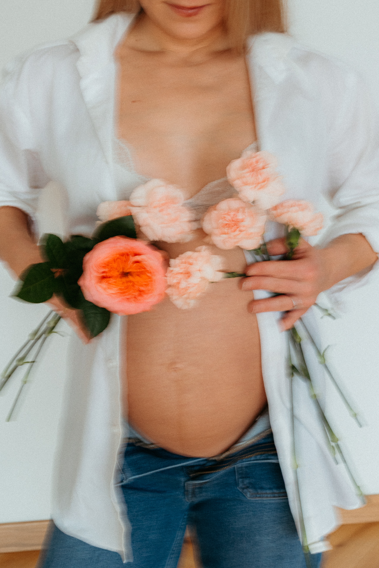 kobieta z odsłoniętym brzuszkiem ciążowym siedzi na podłodze i trzyma róże na brzuszku w domu w Krakowie